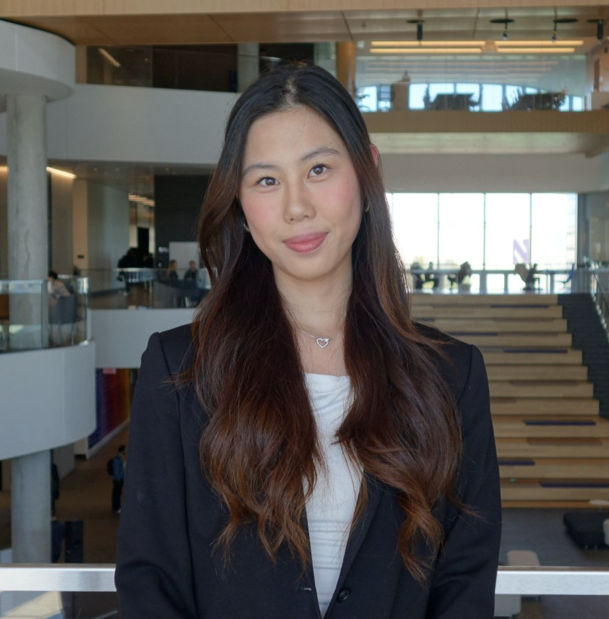 Person in a suit smiling in an indoor setting with modern architecture background.