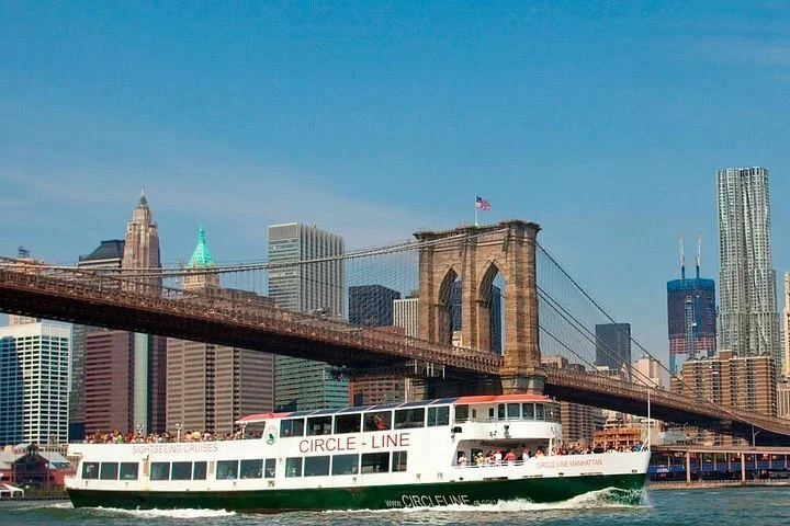 Passeggeri su una nave turistica attraversando il ponte di Brooklyn con lo skyline di Manhattan sullo sfondo.