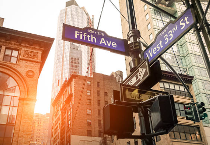 Cartelli stradali all'incrocio tra Fifth Avenue e West 33rd Street in una città con edifici alti, al tramonto.