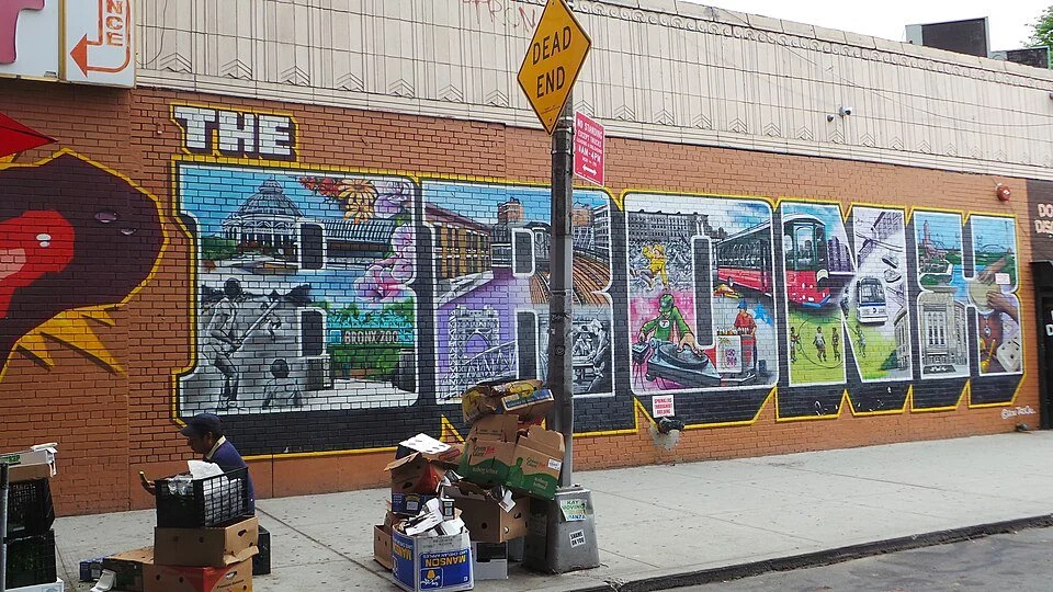 Murale con la scritta 'DRAFT' dipinta su un muro di mattoni, con vari disegni rappresentanti strutture e mezzi pubblici e un cartello stradale con scritto 'DEAD END', in un contesto urbano.