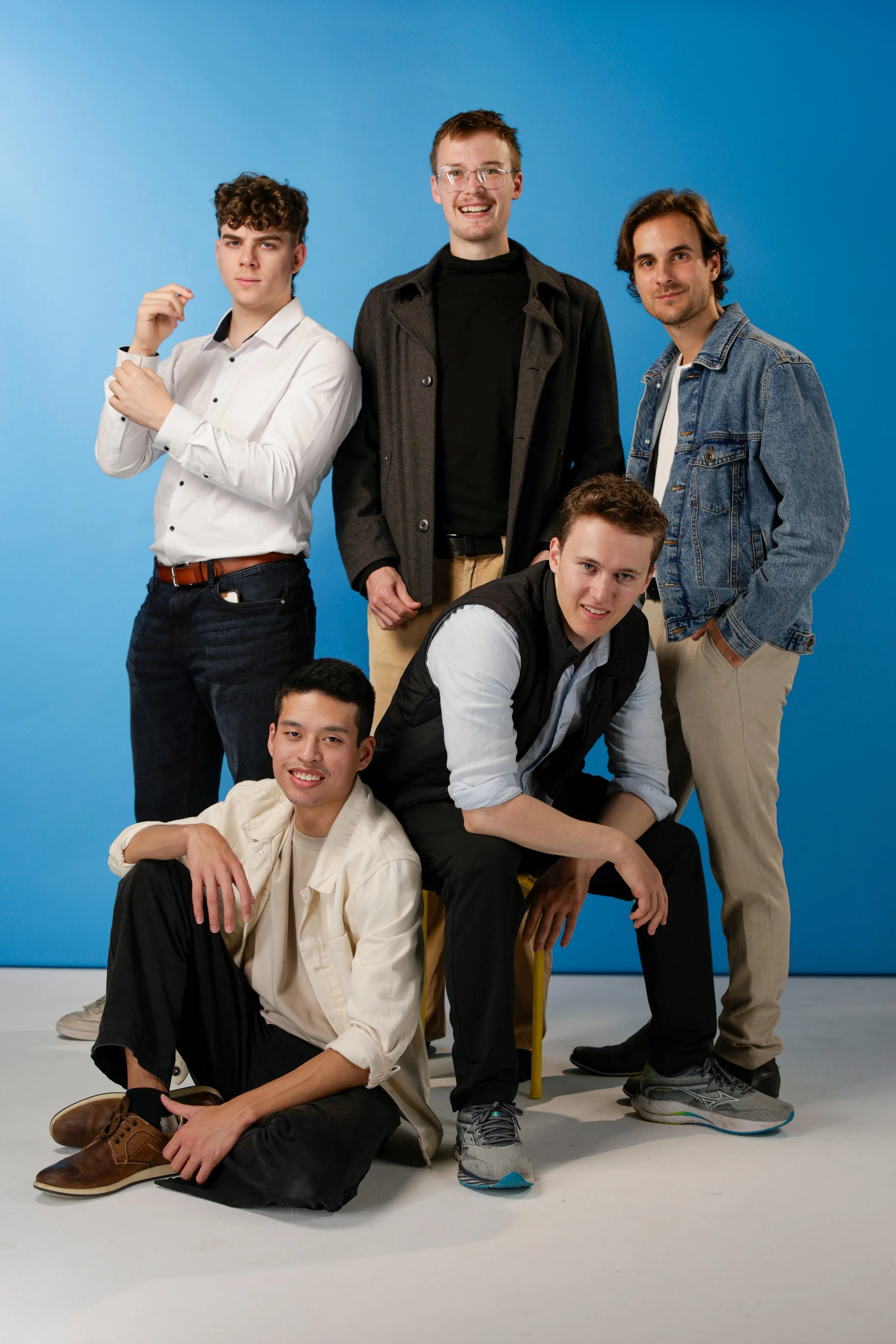 Group of five young men posing together against a blue background.