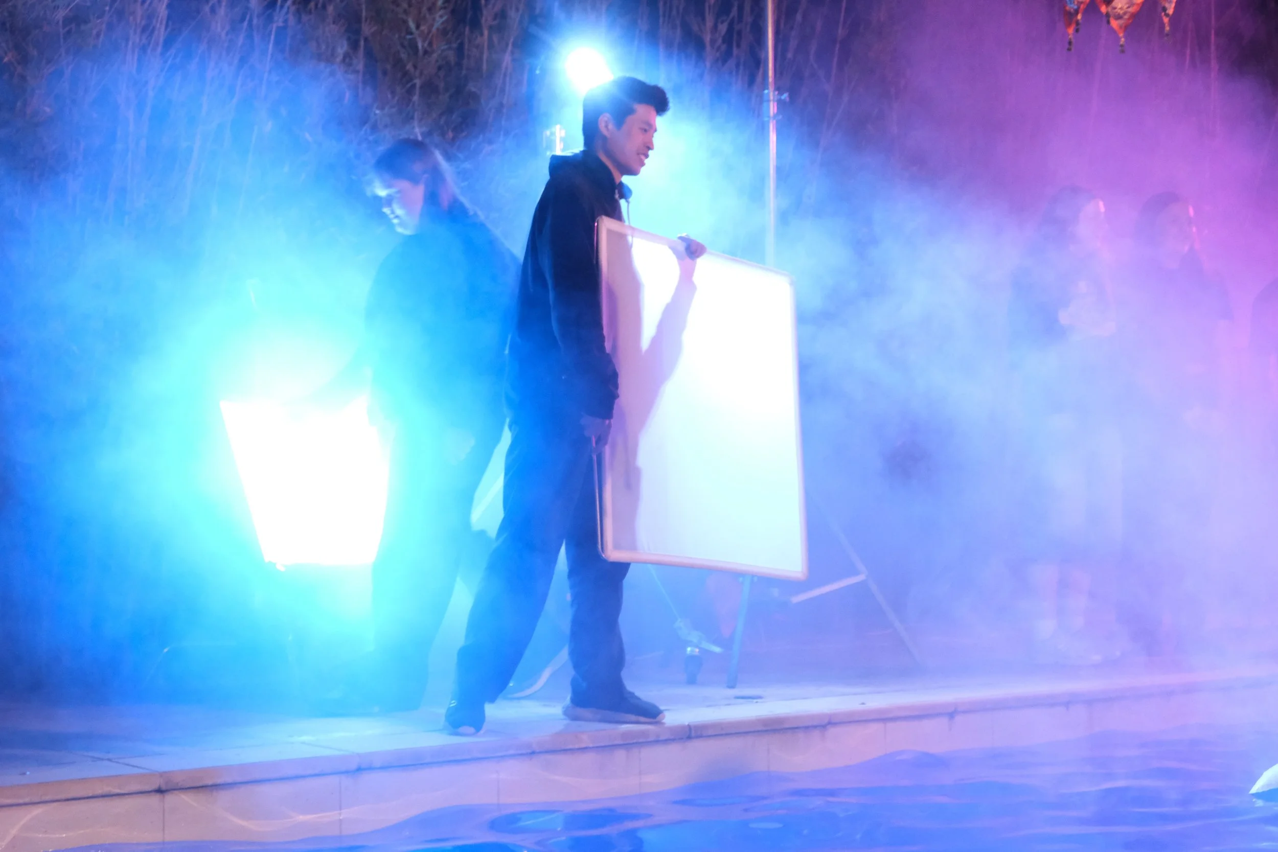 Young man holding a whiteboard on stage with colorful smoke and lights.