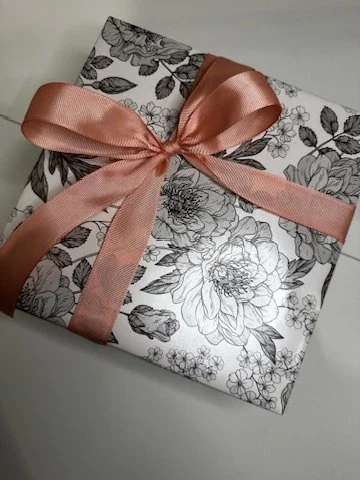 A wrapped gift box with floral black and white pattern, decorated with a pink satin ribbon tied in a bow.