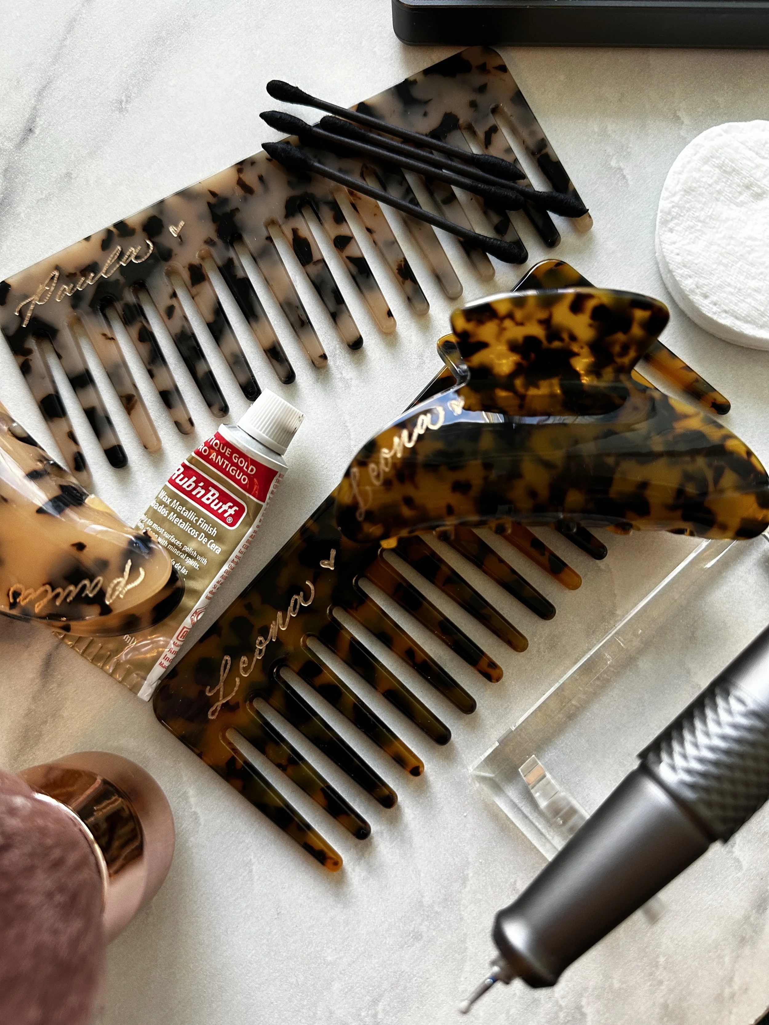 A collection of tortoise-shell hair accessories, including hair clips, a hair comb, and a spray bottle on a white surface. Also visible are a cotton pad and a tube of hair product.
