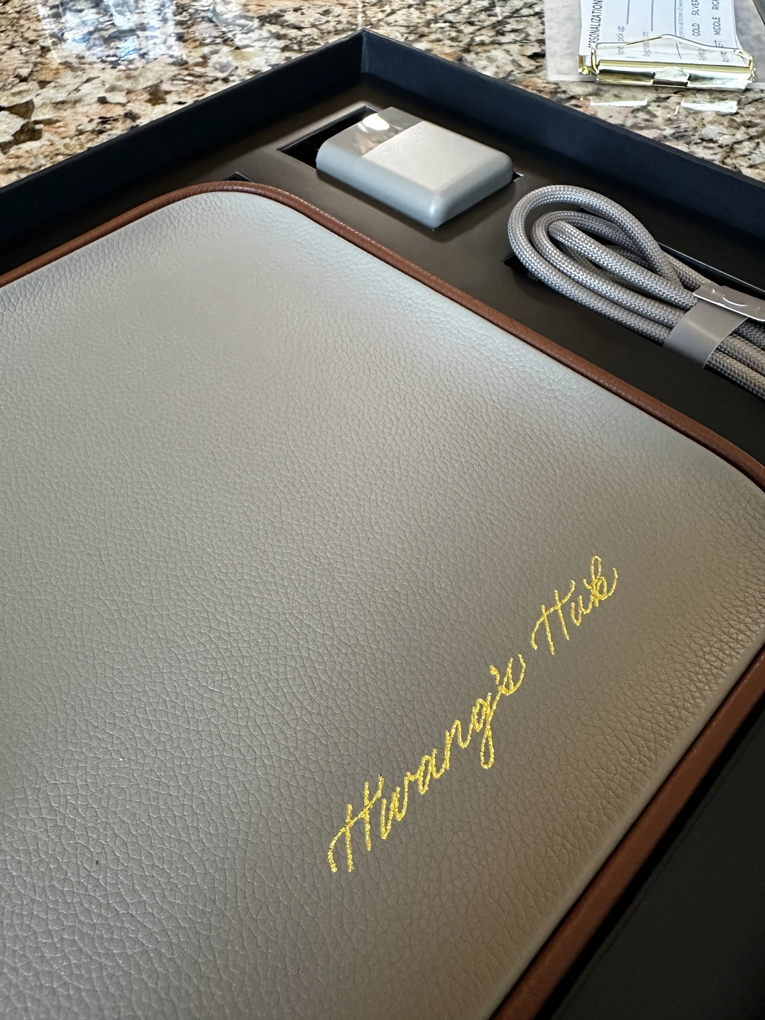 Gold heat foiling written in calligraphy on a beige leather charging pad.