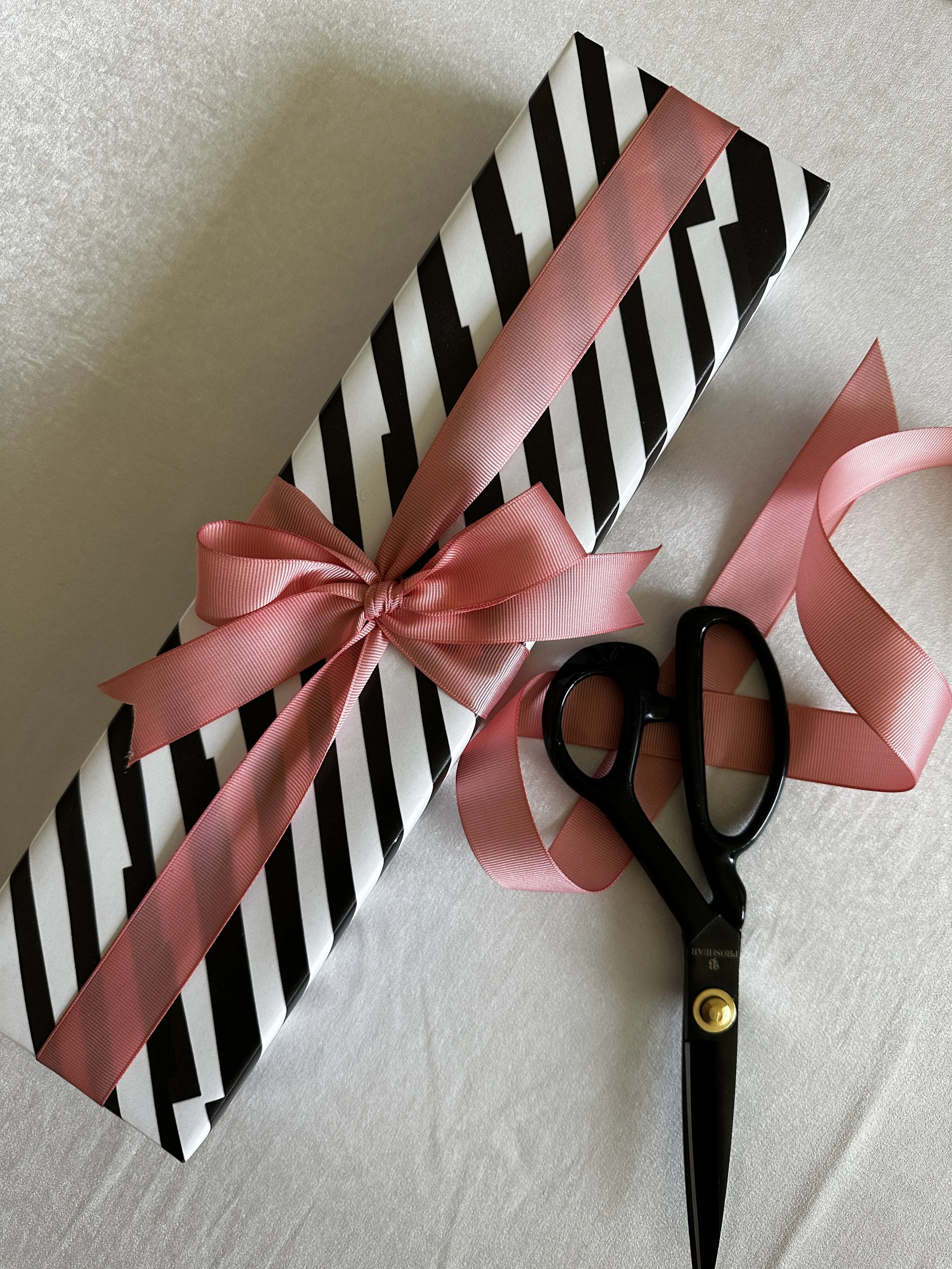 A gift wrapped in black and white striped paper with a pink ribbon tied in a bow, placed next to a pair of black scissors.
