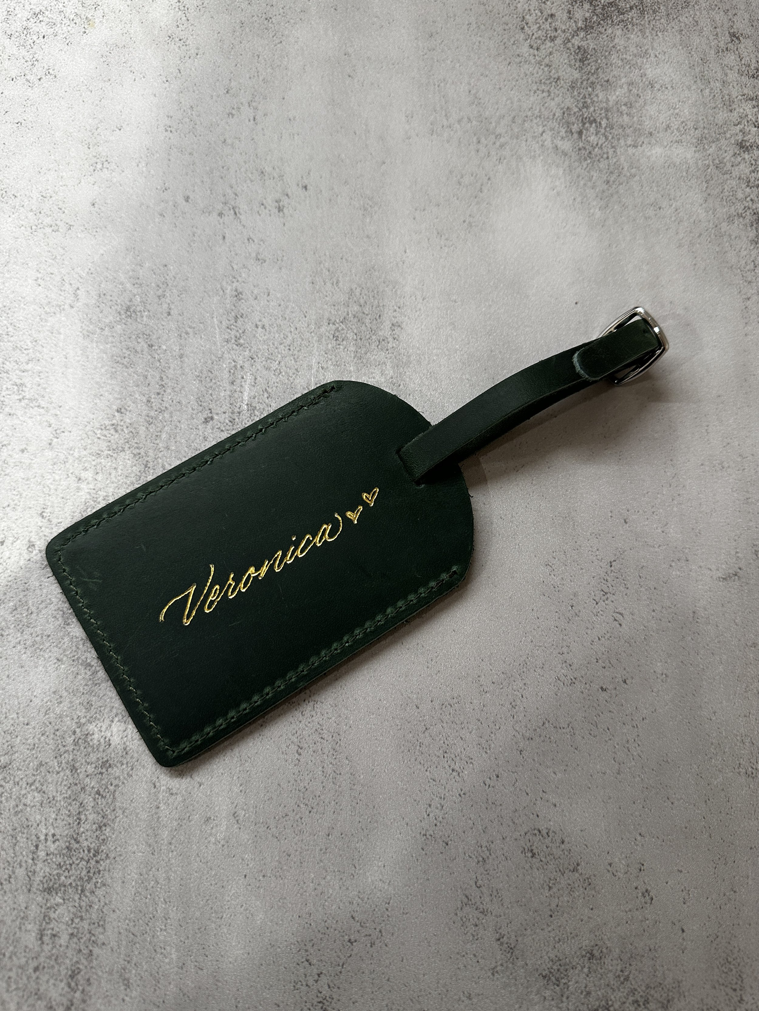 Green leather luggage tag with 'Veronica' written in gold calligraphy.