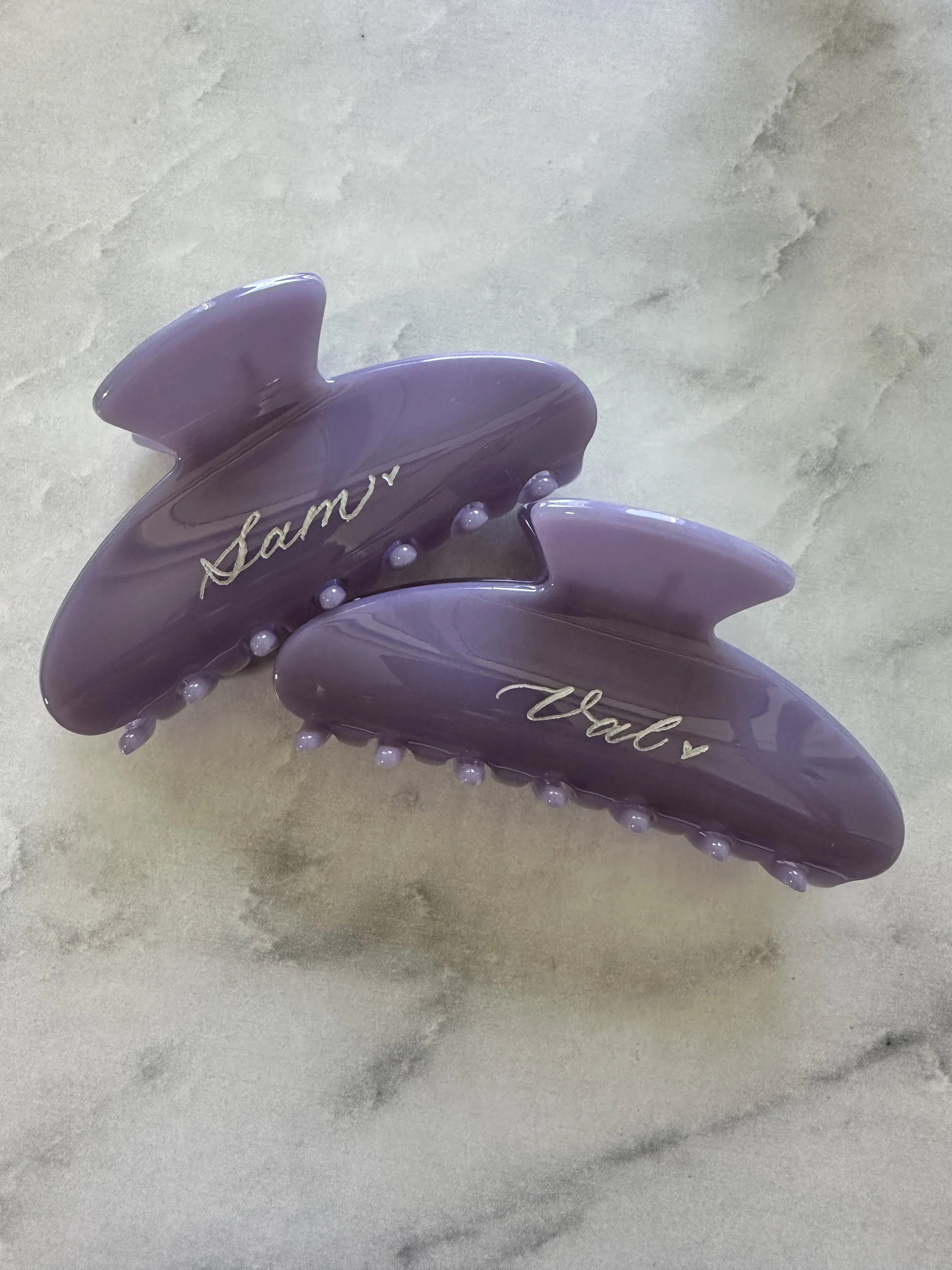 Two hand engraved purple hair clips with the names "Sam" and "Val."