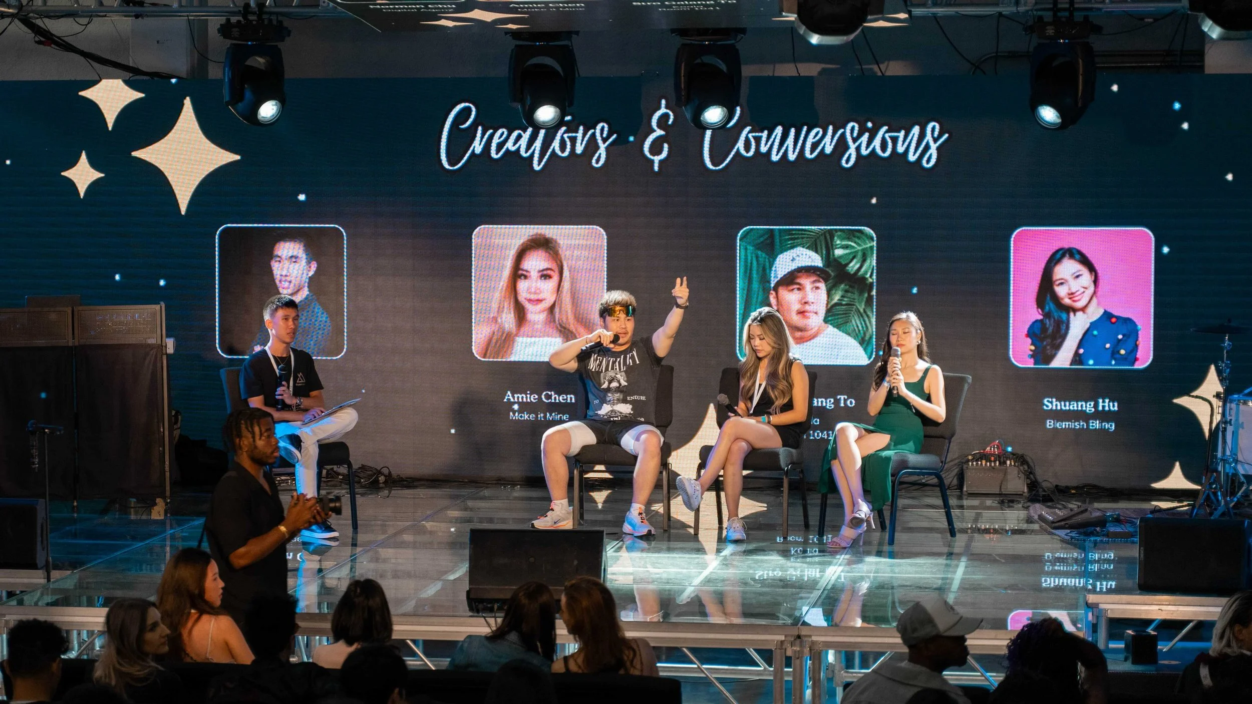 Panel discussion on stage titled 'Creators & Conversions,' with four individuals seated and engaged in conversation, large digital screen behind displaying photos and names of three creators.