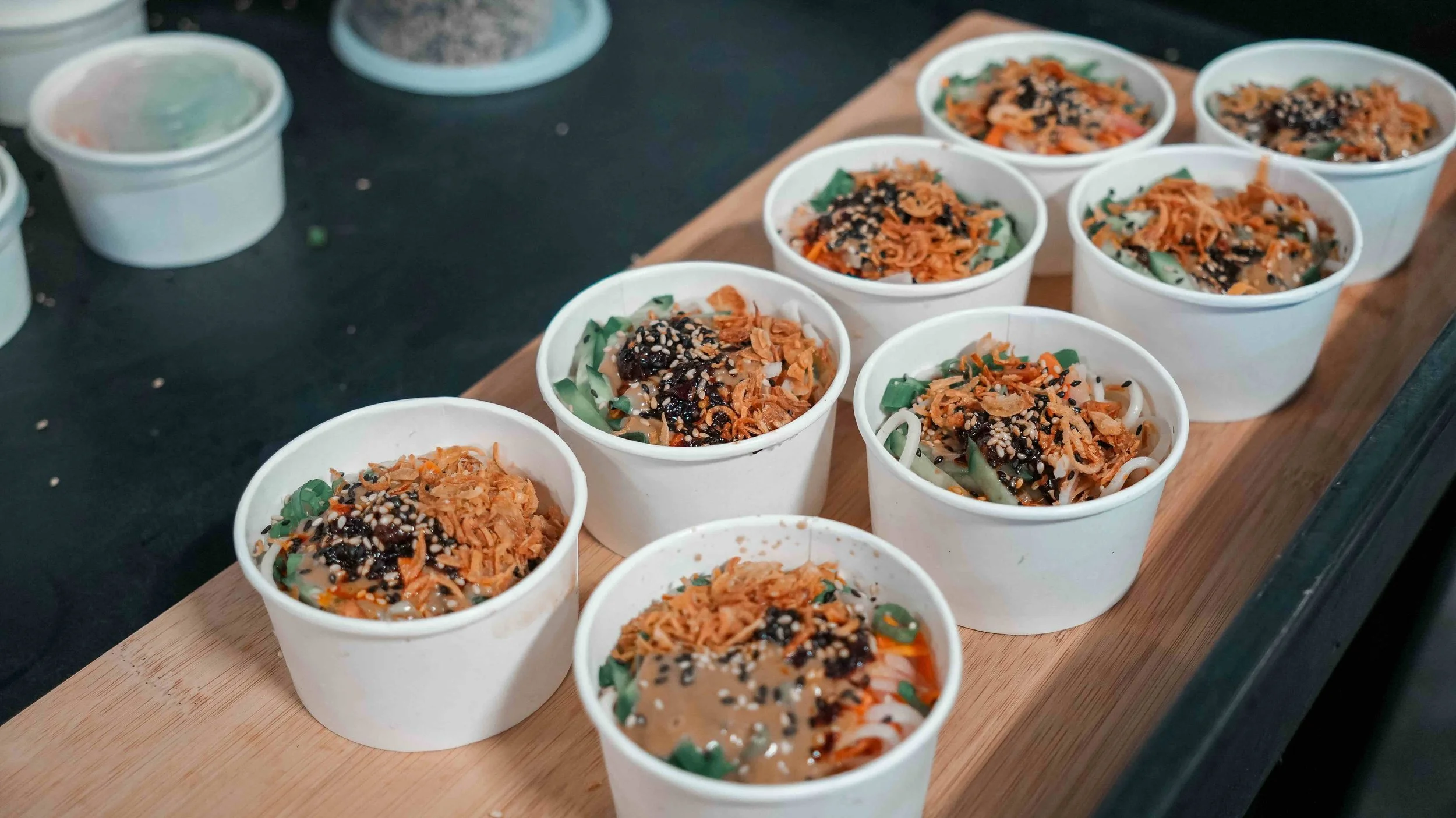Multiple bowls of Asian noodle soup with vegetables and toppings on a wooden serving board.