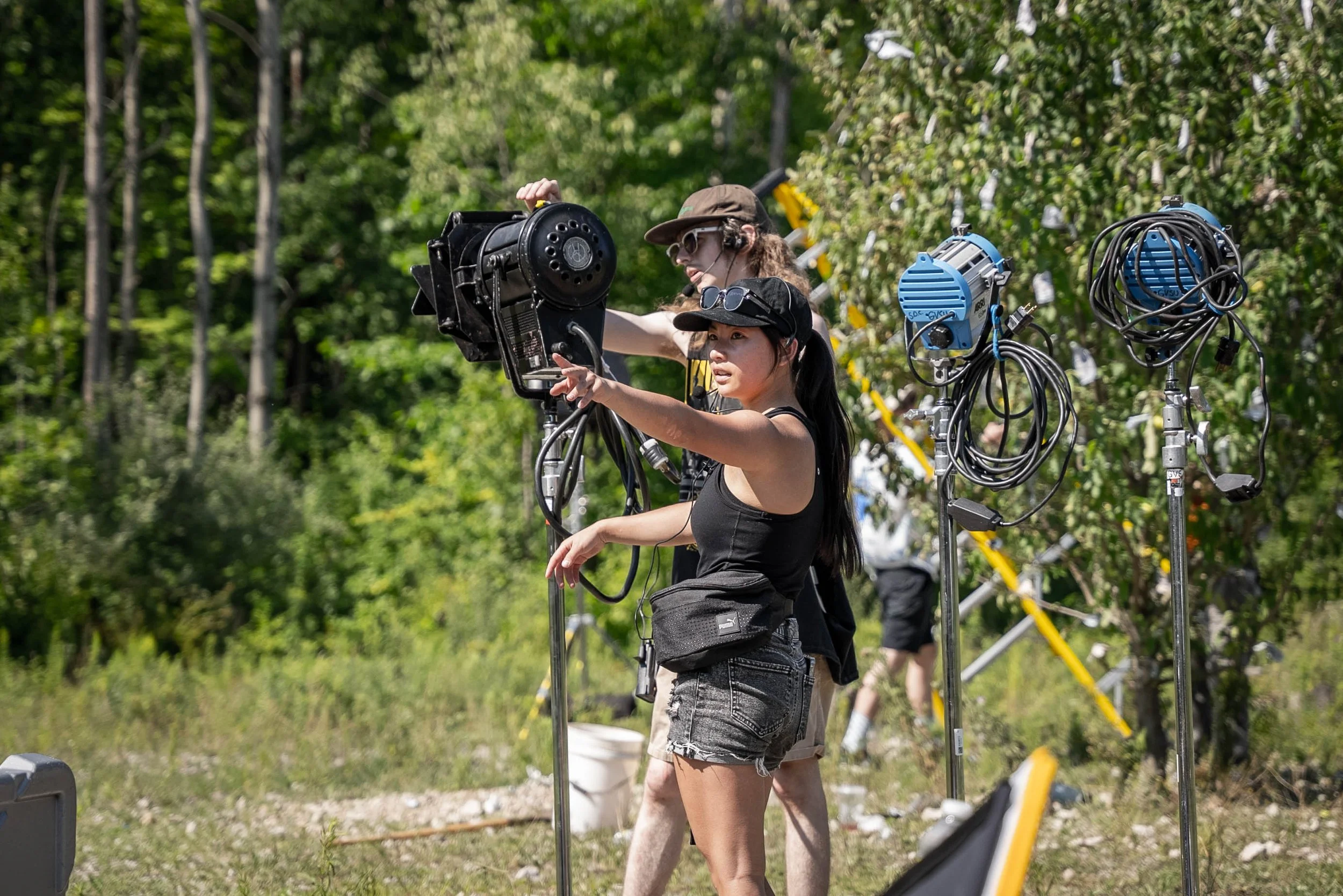 A man and a woman  operating film or photography equipment outdoors among trees and greenery.