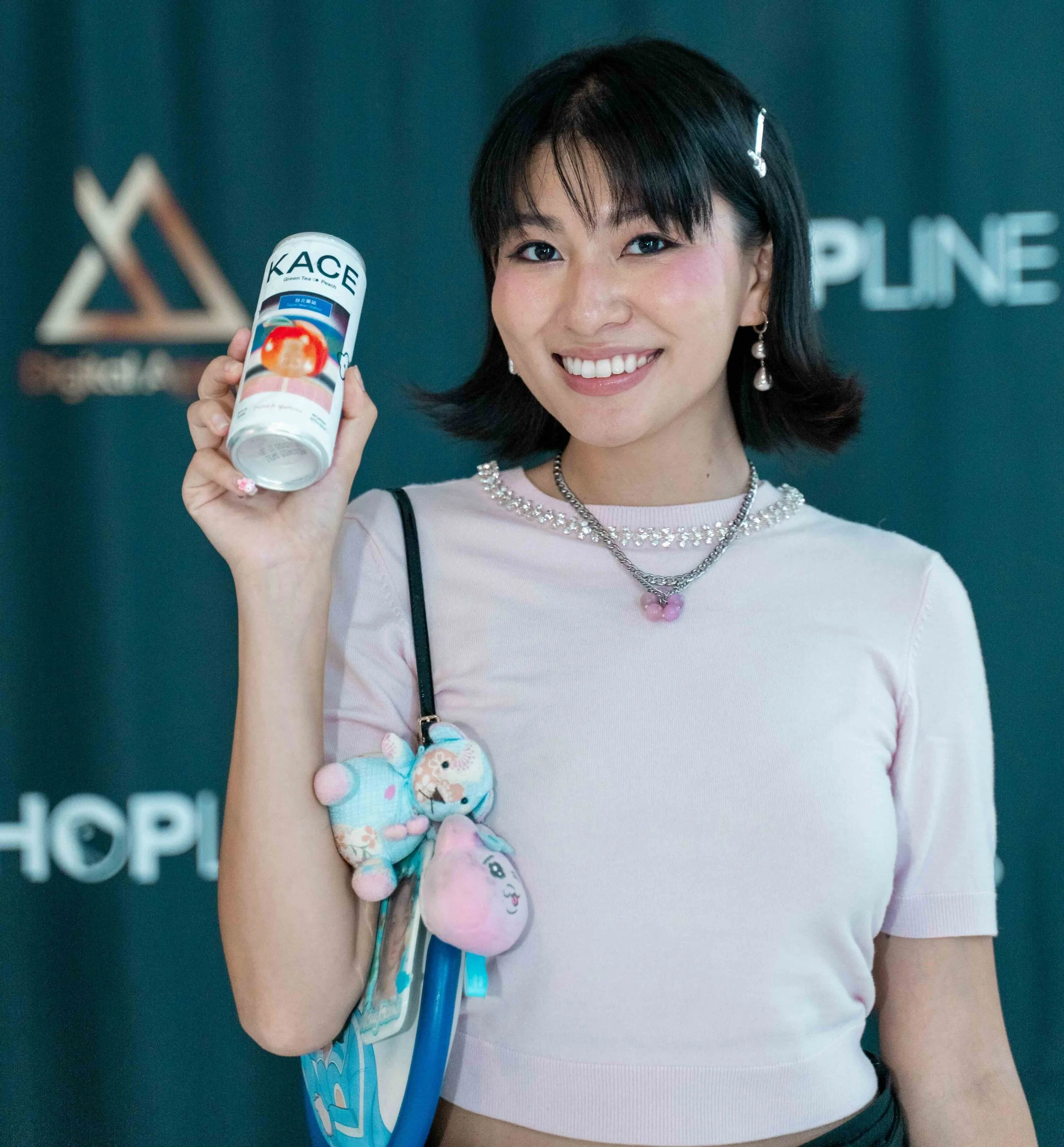 A young woman with black hair and dressed in a pink top smiling and holding a bottle of KACE supplement with a branded background.