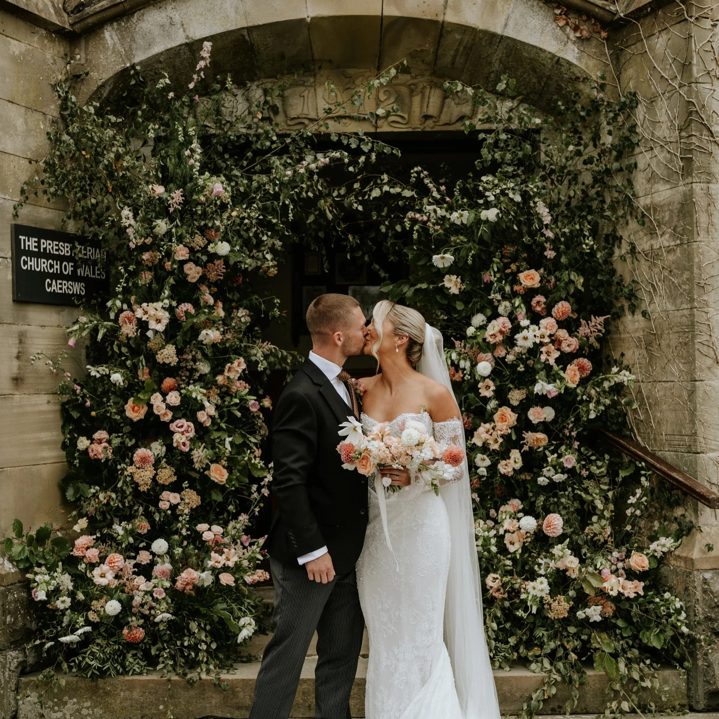 Couple kissing with a blush floral backdrop at a church wedding ceremony.