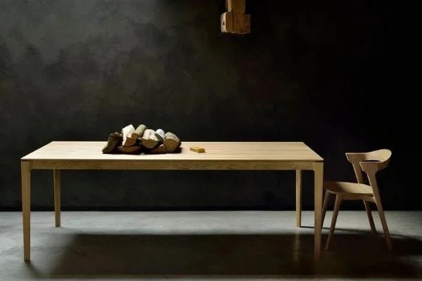 Wooden dining table with rocks on top, in a dark room with a black wall, and a wooden chair on the right side.