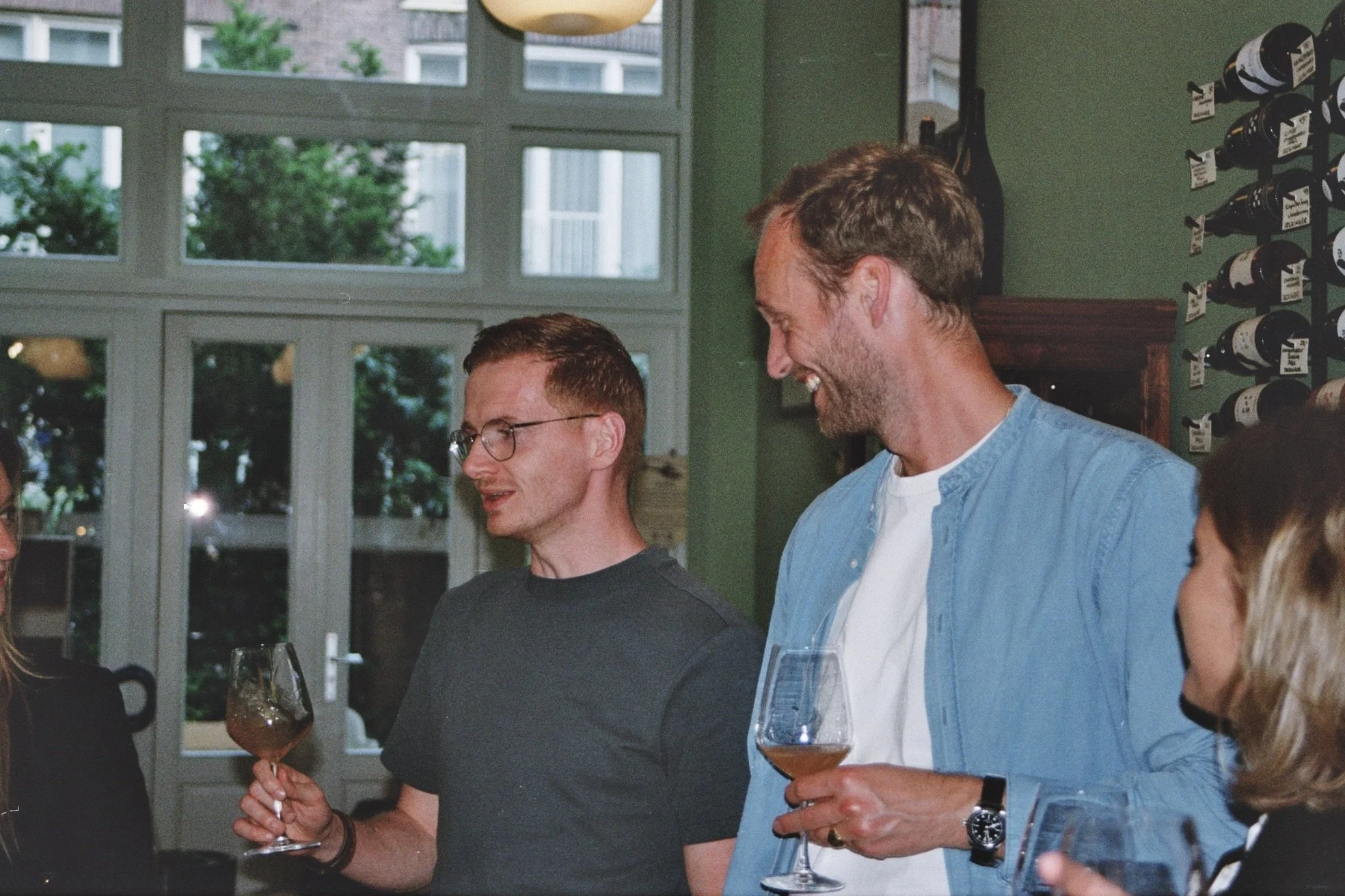 People socializing indoors, holding glasses of wine, smiling and talking.