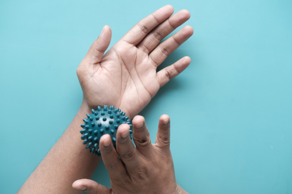 Hand die een blauwe, spijkerharde massagebal vasthoudt op een lichtblauwe achtergrond.