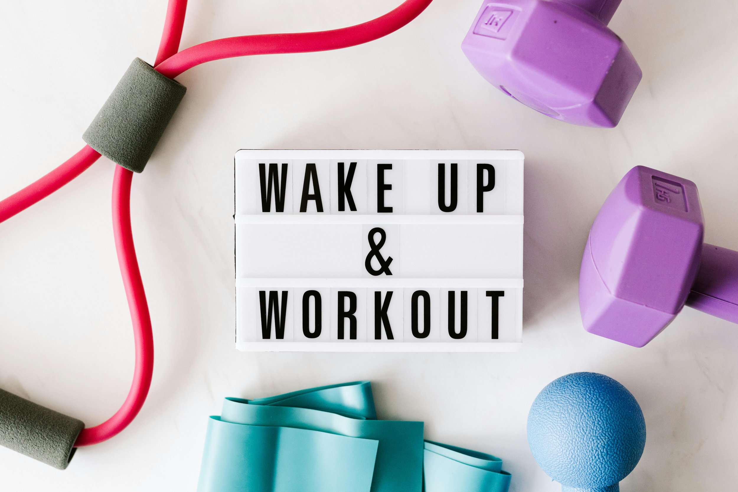 Fitness accessoires zoals dumbbells, een springtouw, een weerstand band en een foam roller, met een lichtbox met de tekst 'WAKE UP & WORKOUT'.