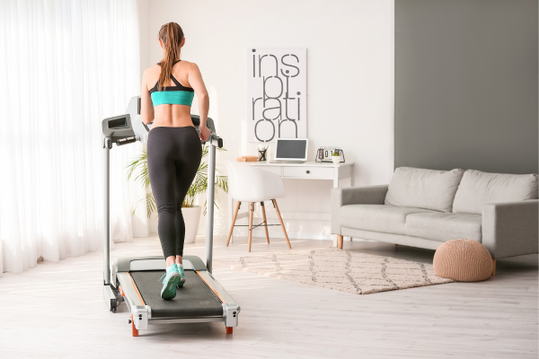 Vrouw die jogt op een loopband in een lichte, moderne woonkamer met wit meubilair en een grijze muur.