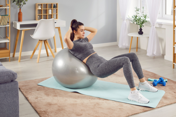 Vrouw die op een yogabal ligt en oefeningen doet in een woonkamer met licht interieur.
