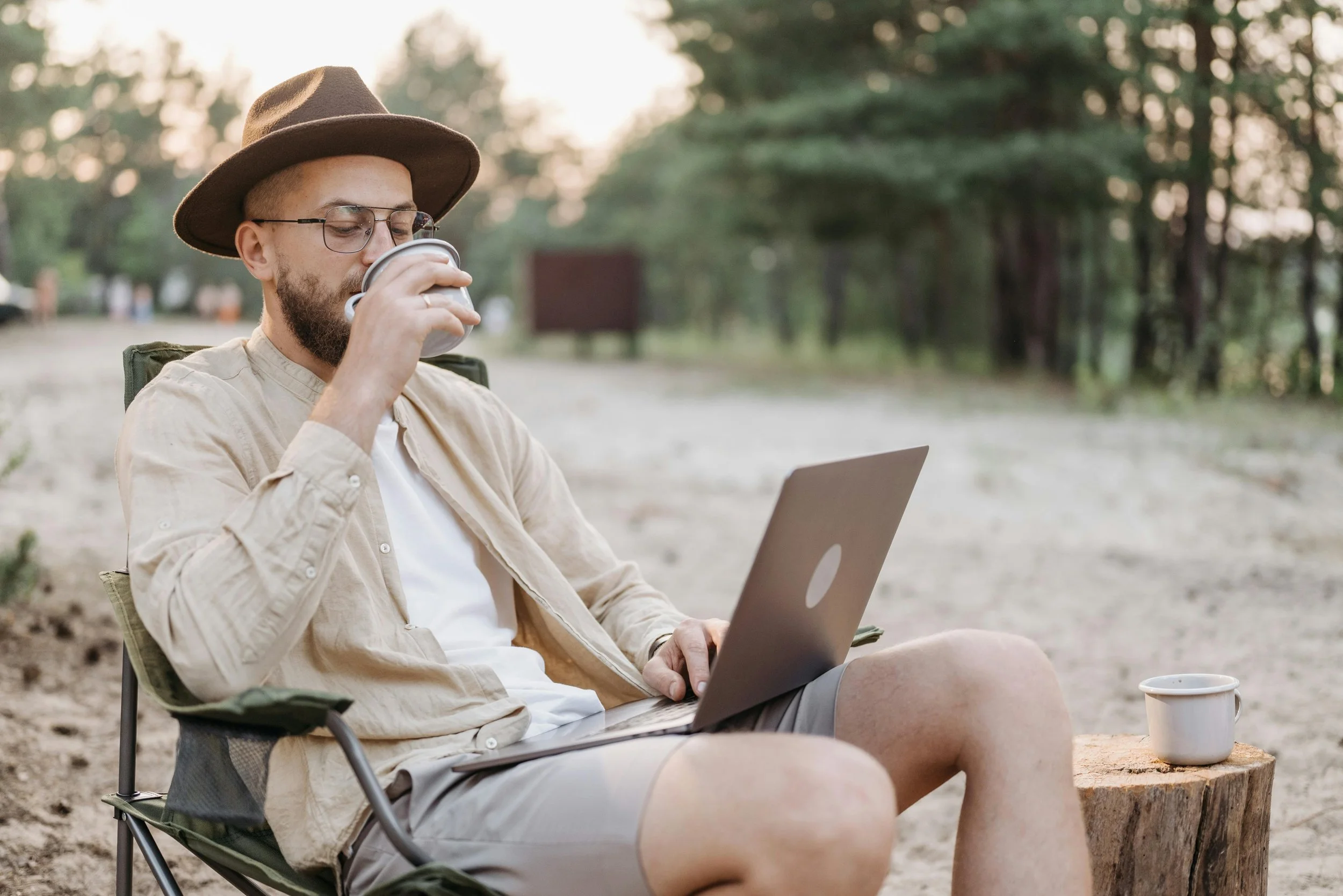 Man using a laptop while drinking coffee in a peaceful outdoor setting – symbolising the ease and flexibility of online ADHD and autism assessments.