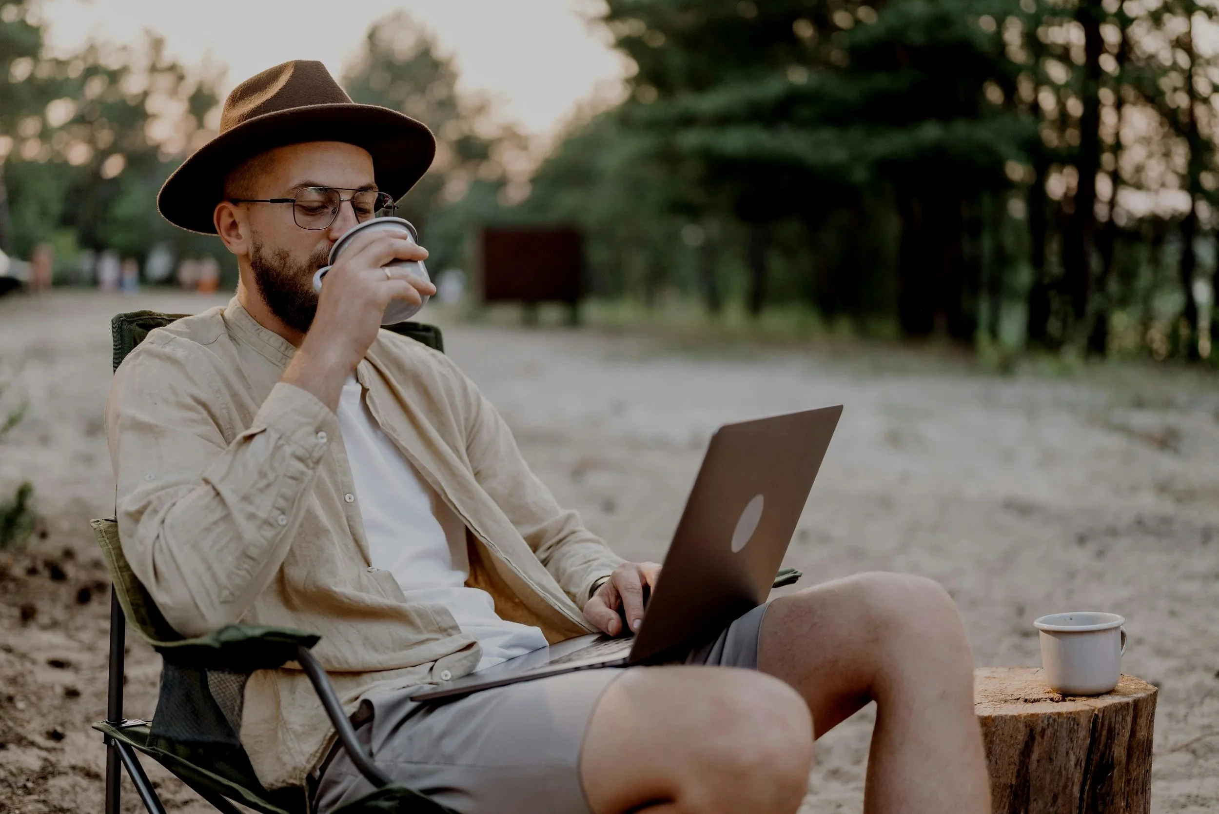Man using a laptop while drinking coffee in a peaceful outdoor setting – symbolising the ease and flexibility of online ADHD and autism assessments.