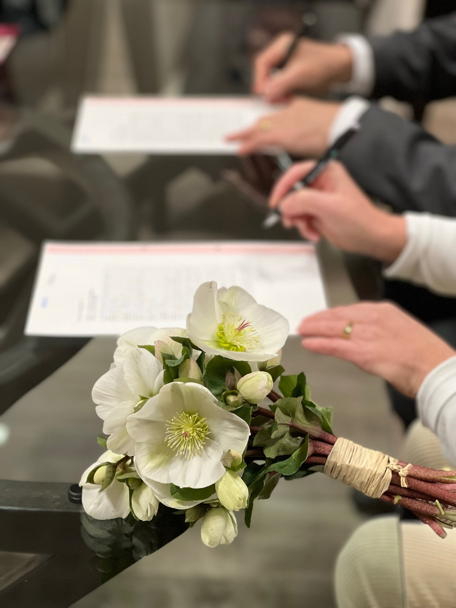 Un bouquet de fleurs blanches sur une table, avec des personnes qui prennent des notes en arrière-plan.