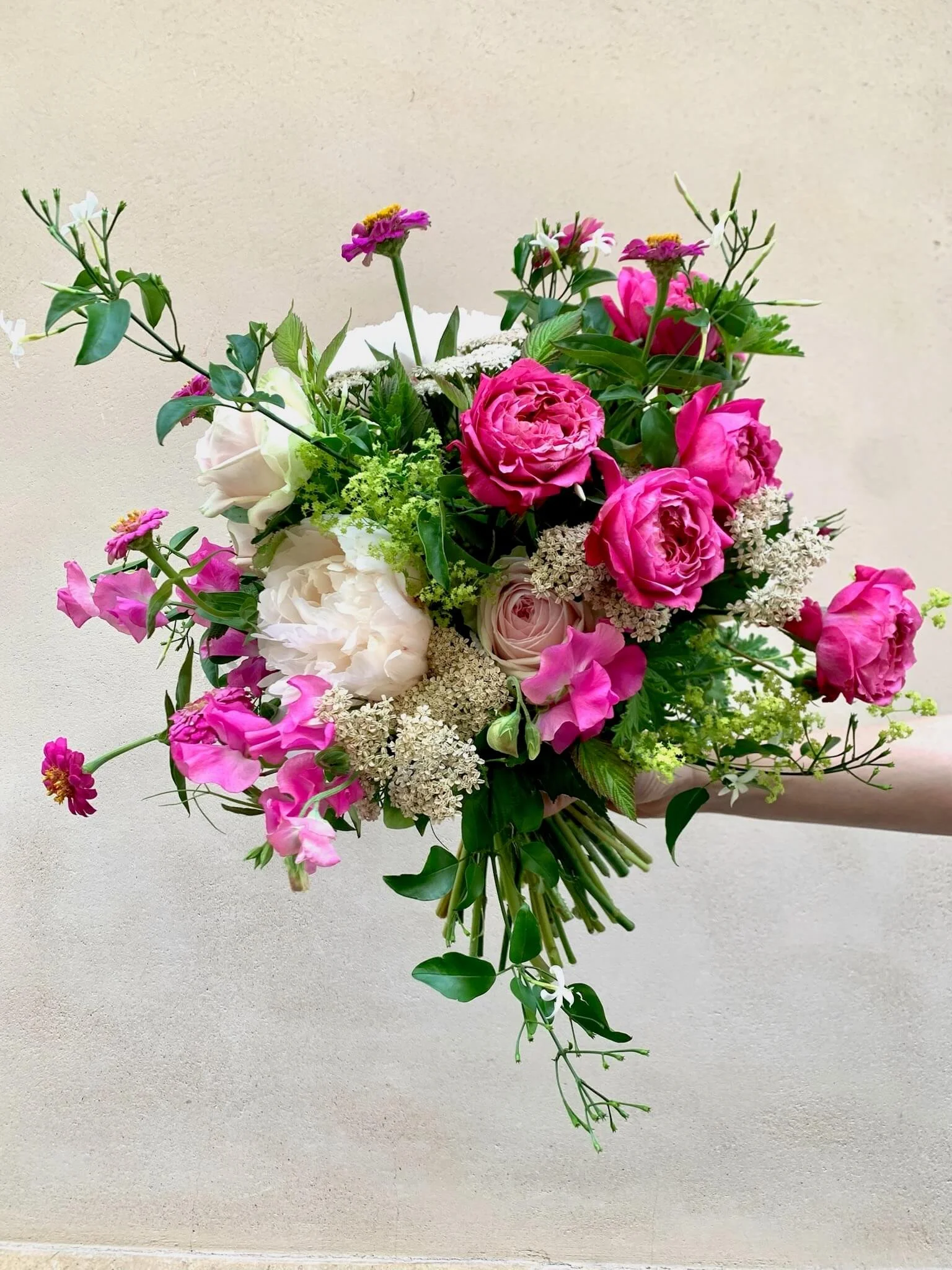 Un bouquet de fleurs composé de roses, de pivoines, de fleurs blanches et de verdure.