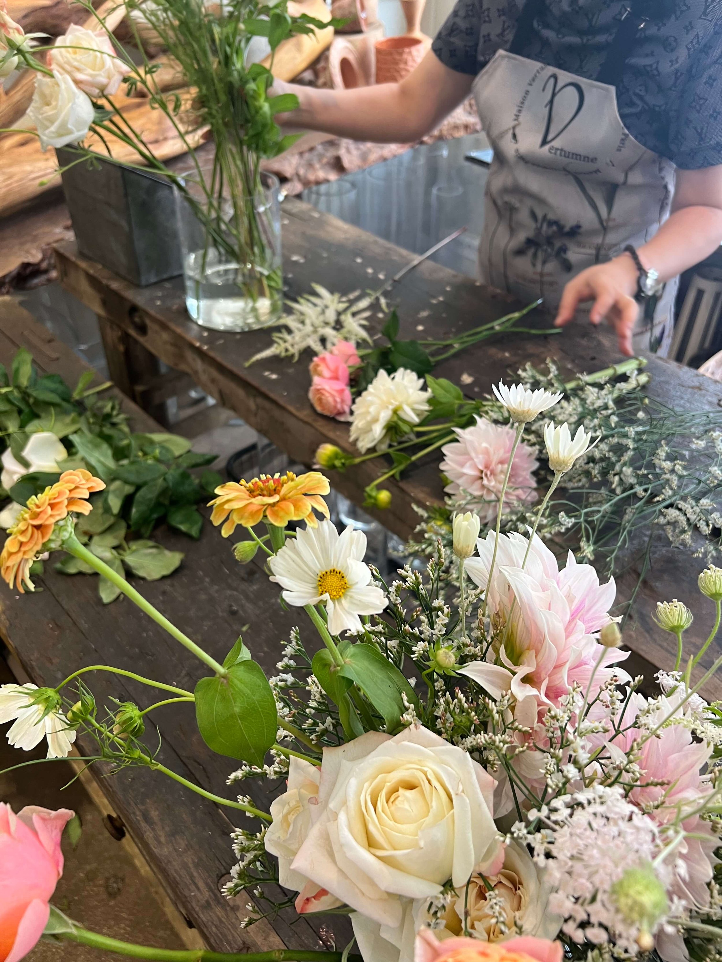Création florale en cours avec fleurs champêtres et gestuelle précise. Atelier encadré dans une ambiance douce.