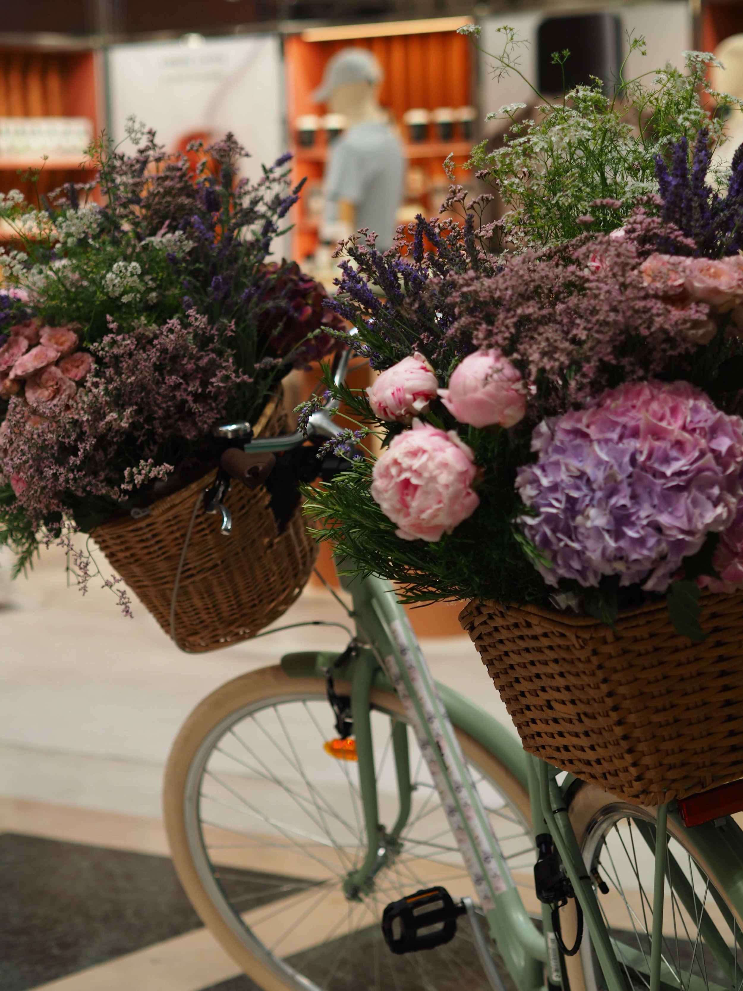 Un vélo avec deux paniers garnis de fleurs, situé en intérieur.