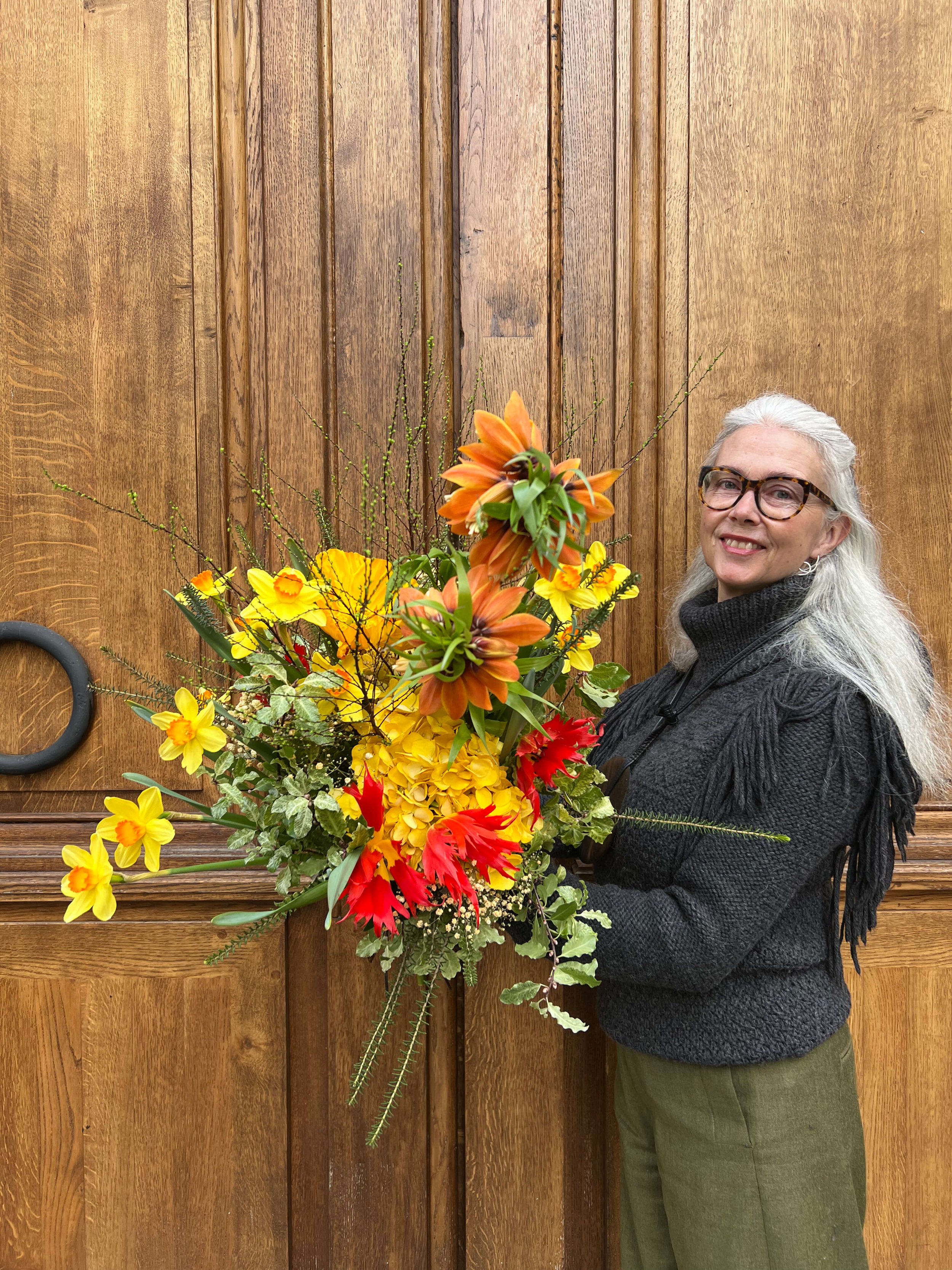 Composition lumineuse aux tons jaune et orange, photographiée devant une porte en bois. Un bouquet plein d’énergie et de caractère.