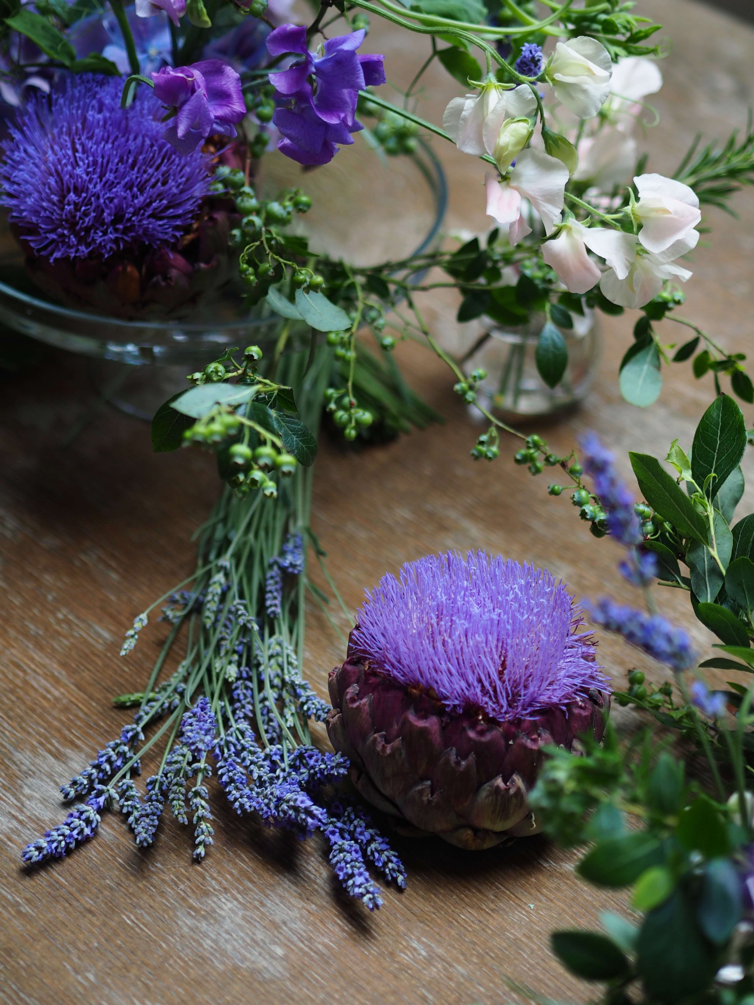 Un bouquet de fleurs violettes, blanches et vertes sur une table en bois, avec une artichaut violet au centre.