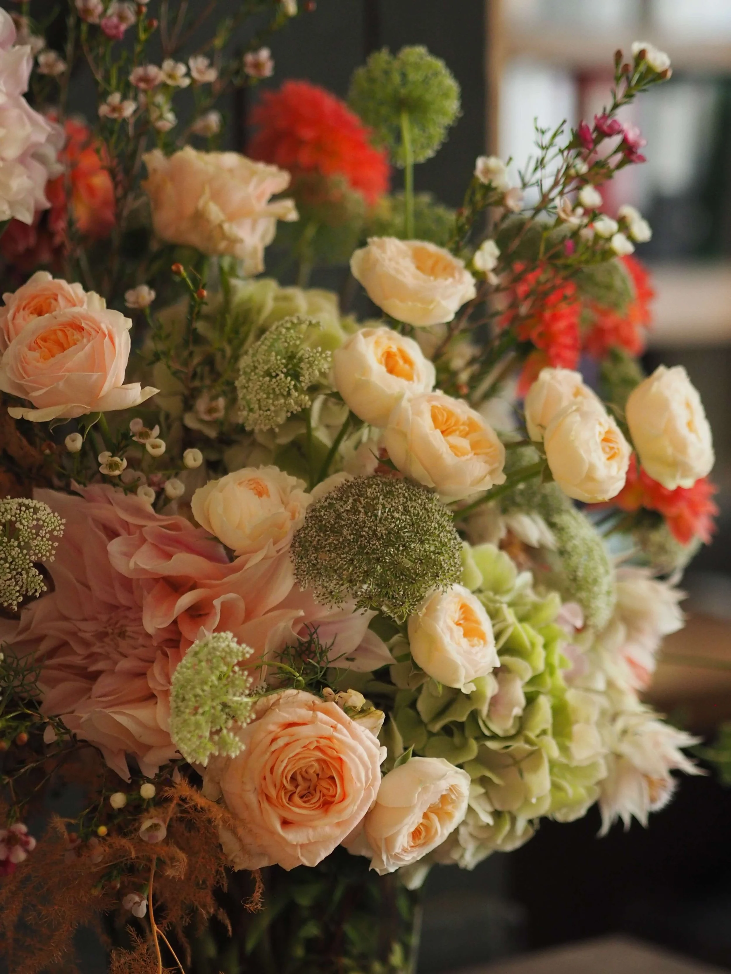 Un bouquet de fleurs comprenant des roses, des hortensias, et diverses fleurs sauvages dans des tons pastel et crème.
