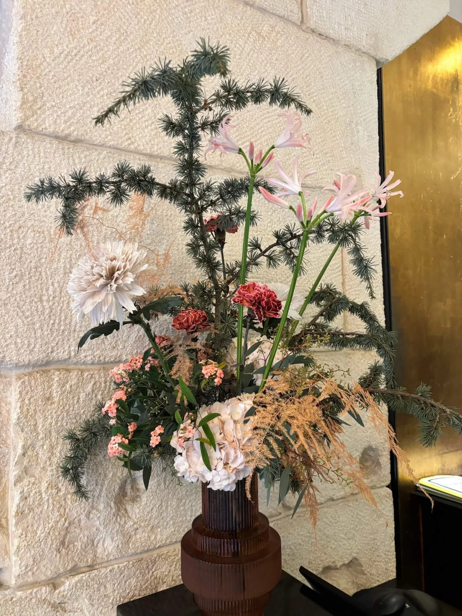 Arrangement floral avec des fleurs roses, blanches et rouges dans un vase en bois, placé contre un mur en pierre.