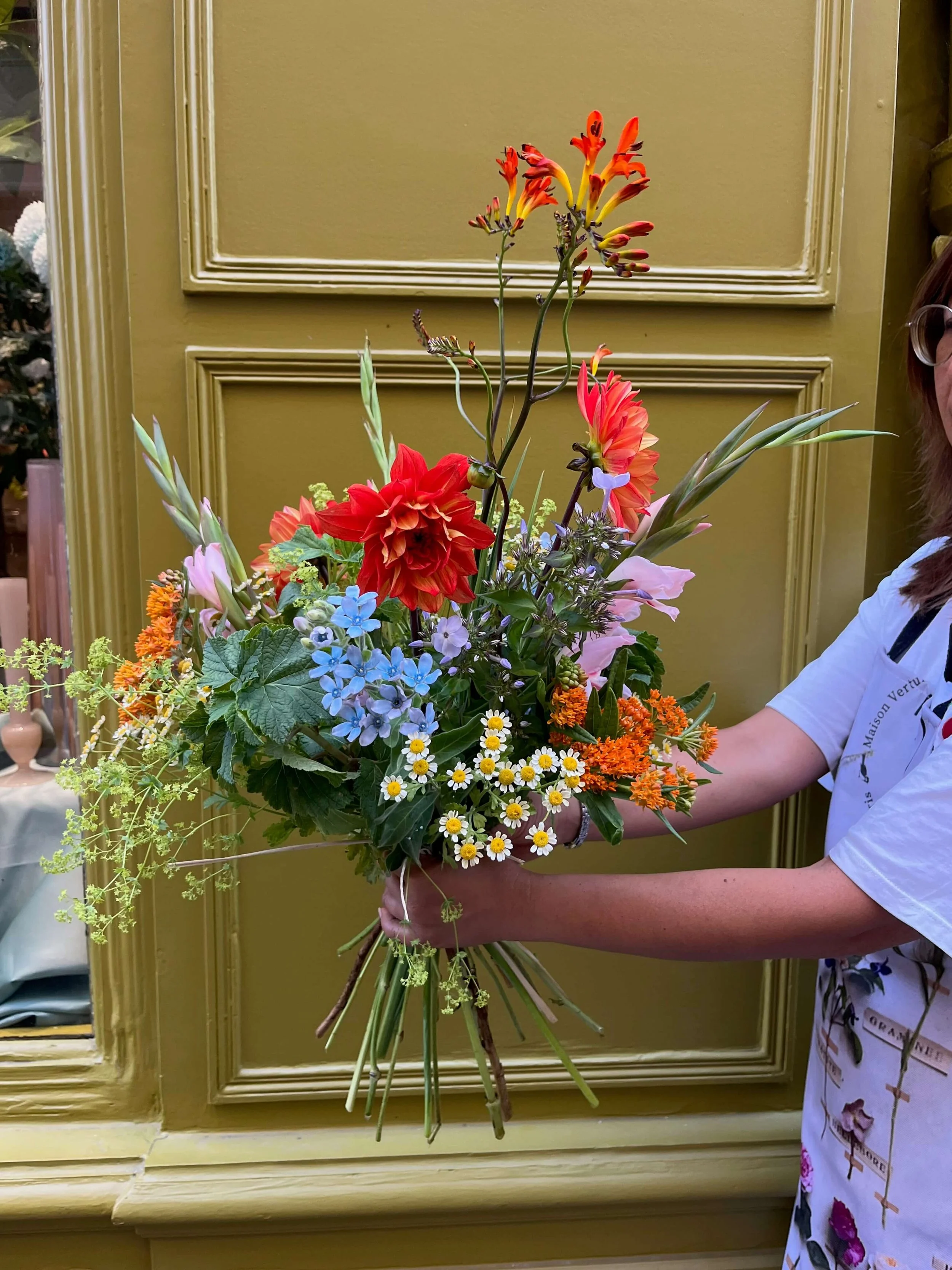 Personne tenant un bouquet de fleurs colorées devant un mur vert
