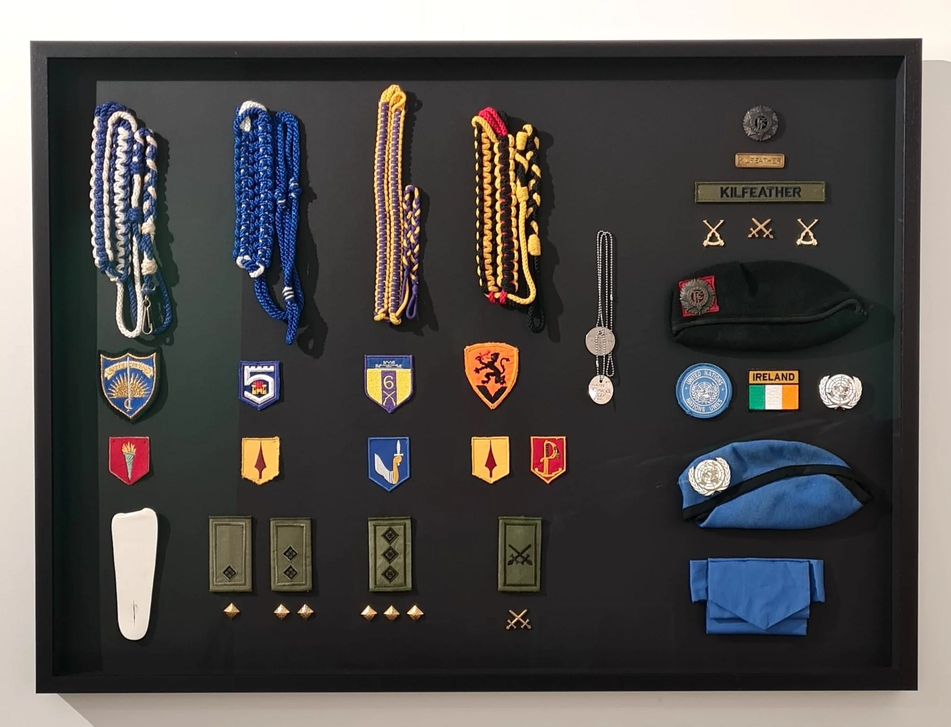 collection of Irish military service insignia, badges, lanyards, rank patches and UN berets, shadow-box framed in black by Image Framers, Sligo