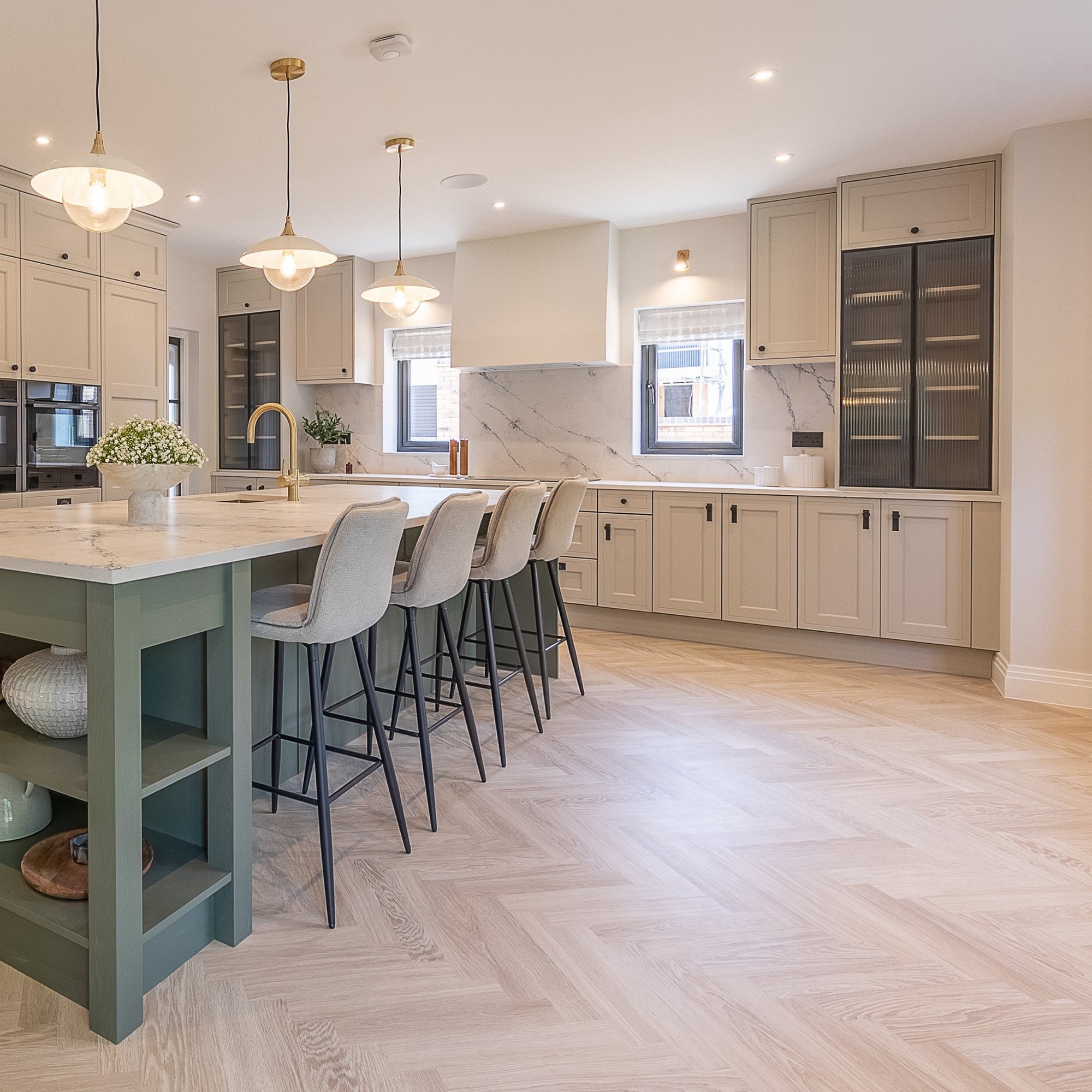 Modern kitchen interior with an island, bar stools, pendant lights, and beige cabinetry.