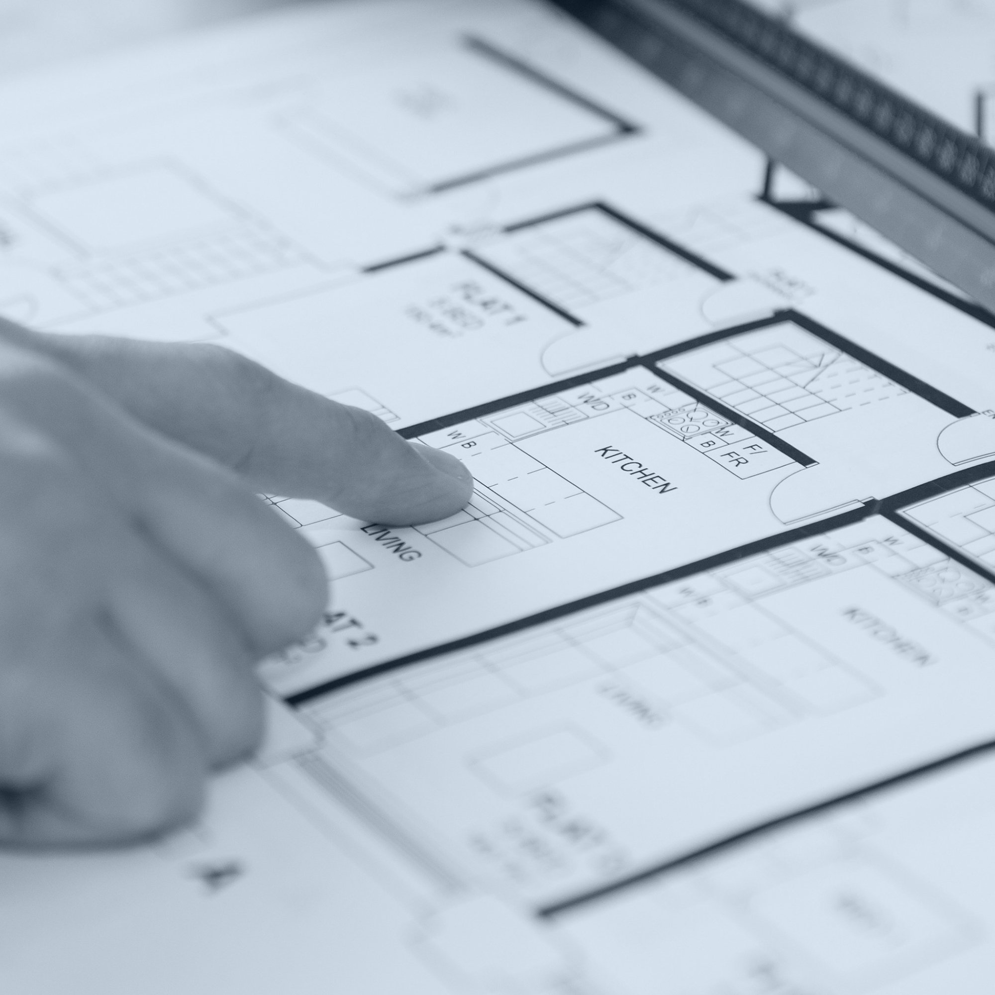 Close-up of a hand pointing at a floor plan blueprint showing a kitchen layout.