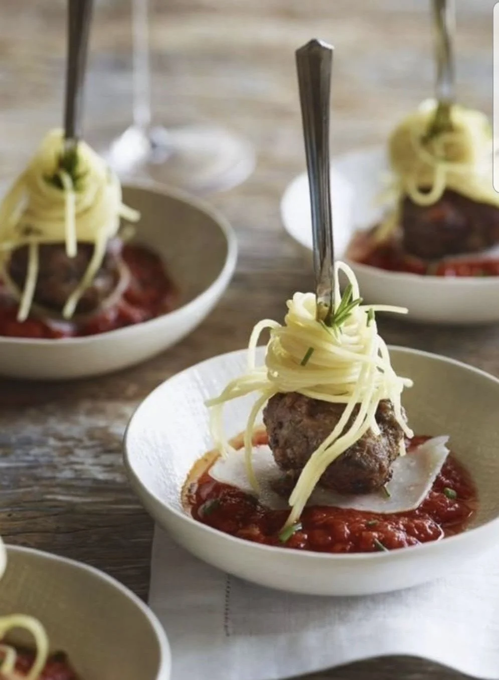 Bord met Italiaanse gehaktballetjes in tomatensaus, gegarneerd met spaghetti, geserveerd in een wit kom, met vork.