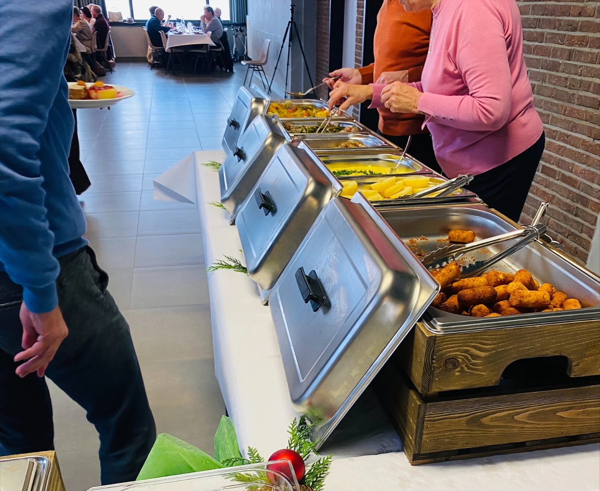 Buffet met verschillende warme gerechten en mensen die eten opscheppen.