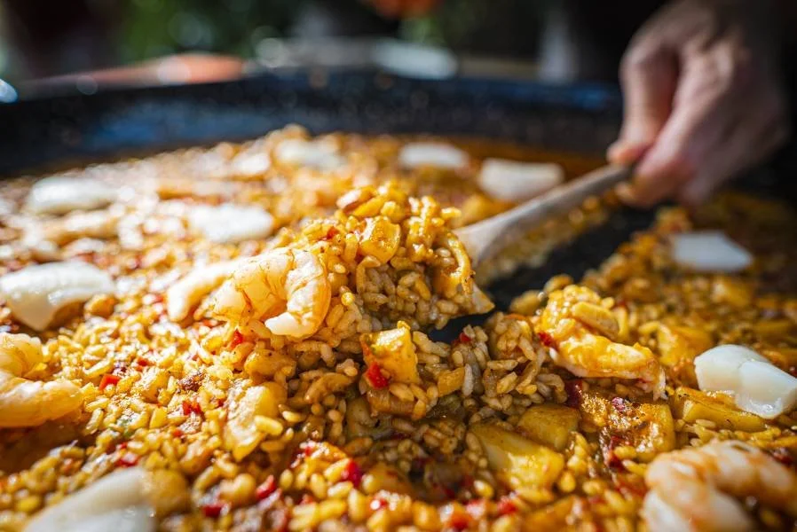 Een grote pan met gebakken rijst, garnalen en groenten, met een lepel die een portie uit de pan schept.