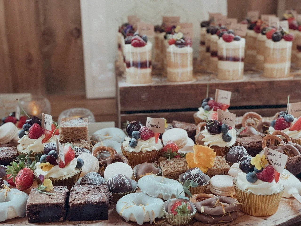 Een tafel met diverse cupcakes, brownies, macarons en vruchtentartes, versierd met fruit en bloemen, in een bakkerij of winkel.