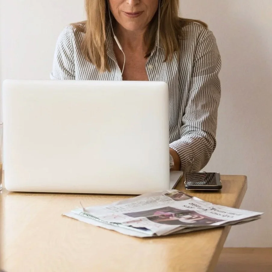 Henkilö istuu sängyllä käyttämässä kannettavaatietokonetta ja pitää kahvikuppia, jossa on koristeellinen maitovalkoinen kuvio.