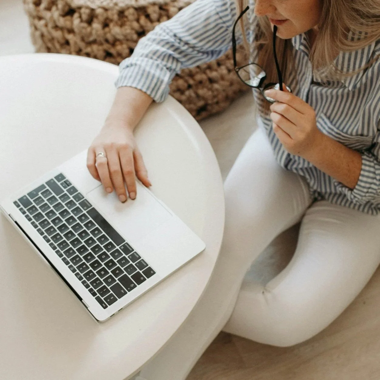 Nainen, joka pitää koria, jossa on asetelma lehtikasveja ja pieniä valkoisia kukkia, katsoo pois päin.