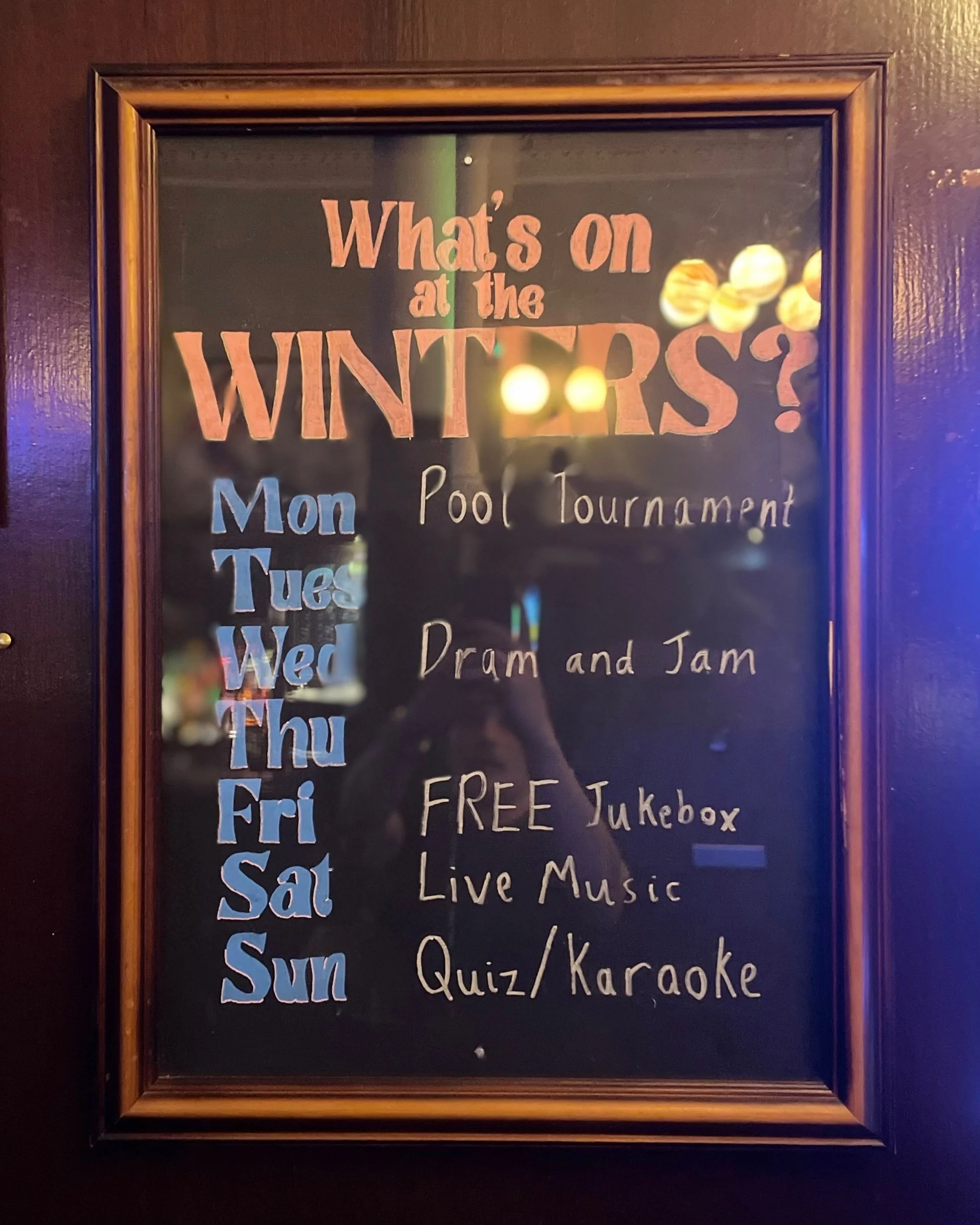 Weekly activities schedule on a blackboard with a wooden frame, listing pool tournament on Monday, drum and jam on Tuesday, free jukebox on Wednesday, live music on Thursday, and quiz or karaoke on Sunday.