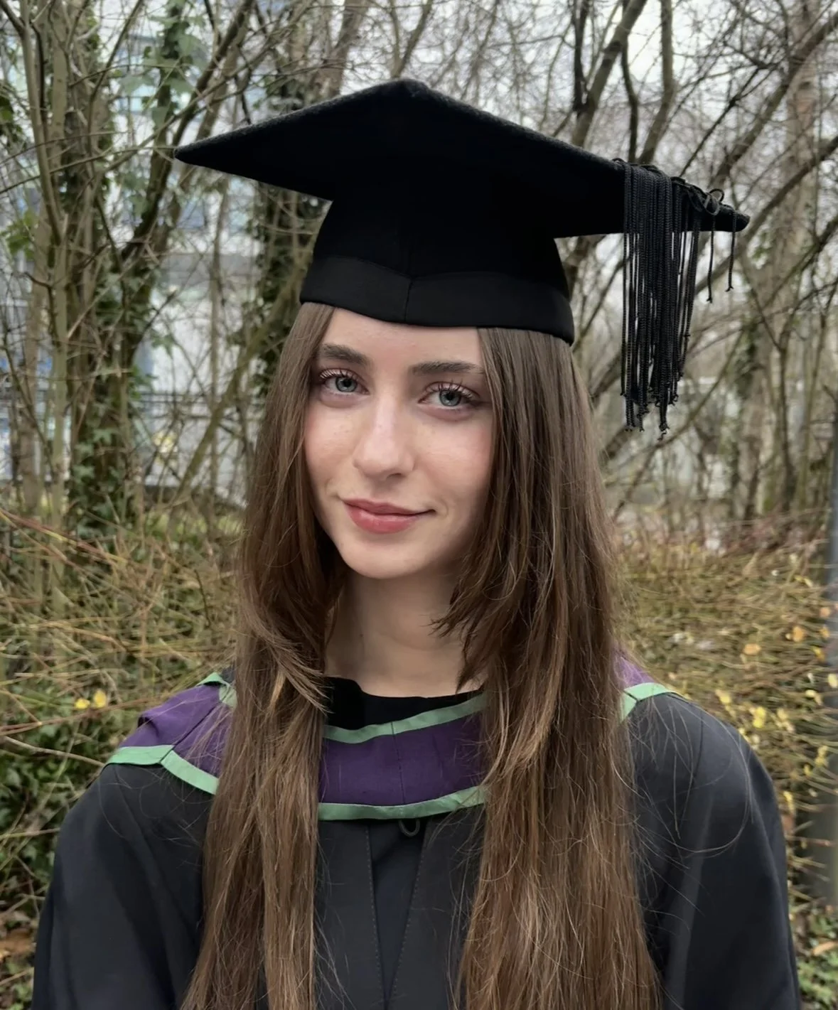 Sadie Grace on her graduattion day, wearing the traditional mortar board and gown, she has long brown hair and has her head tilted slightly