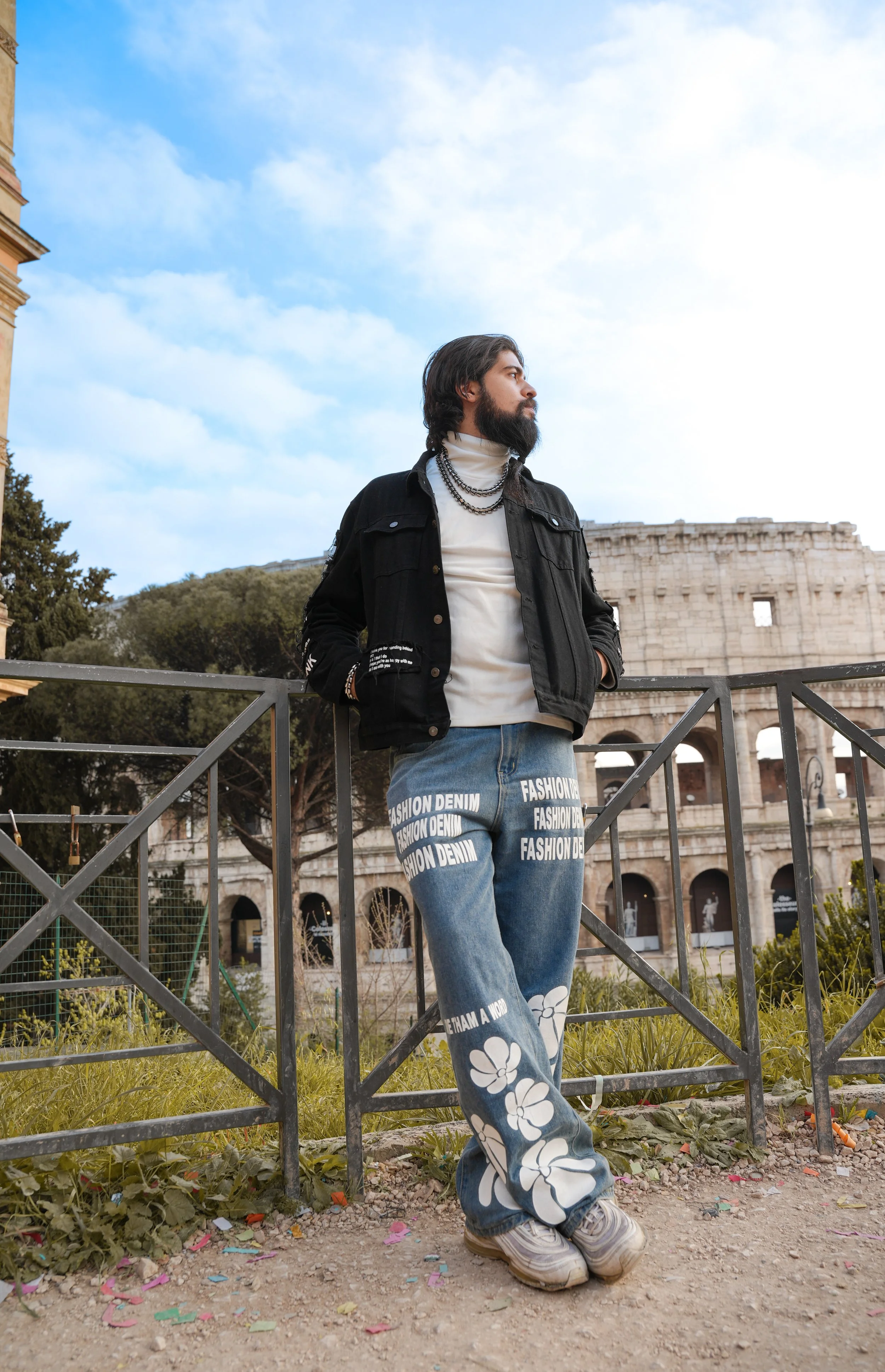 Man in black jacket and jeans with floral design standing near the Colosseum