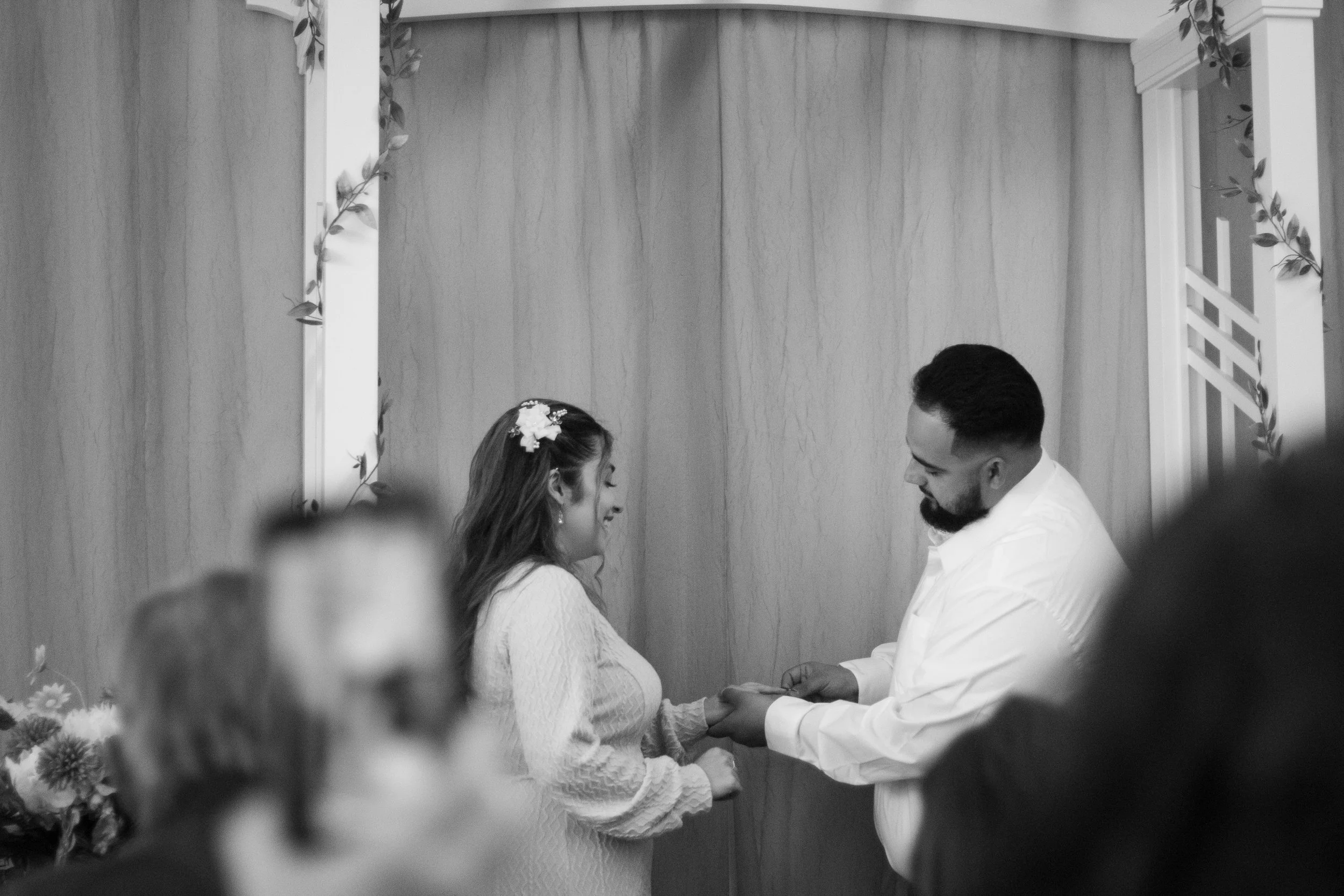 A black and white photo of a couple exchanging rings in a wedding ceremony, standing under a decorated archway In Santa Rosa Ca