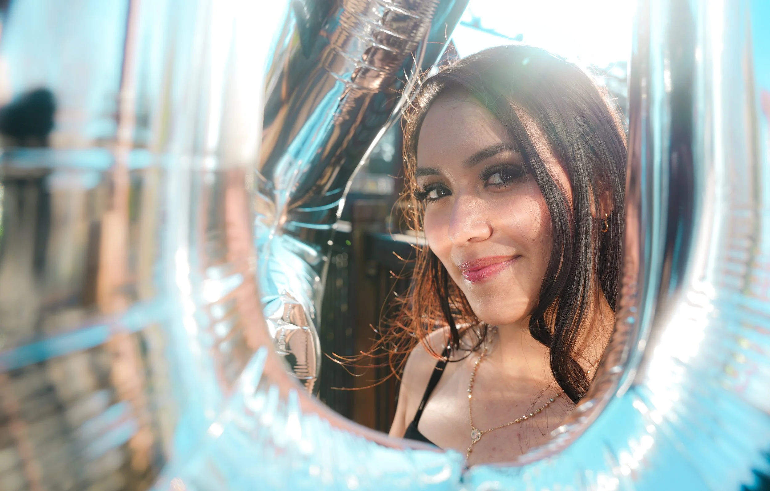 Woman Birthday Photoshoot in downtown Santa Rosa Ca smiling with large shiny balloons in background, sunlit setting.