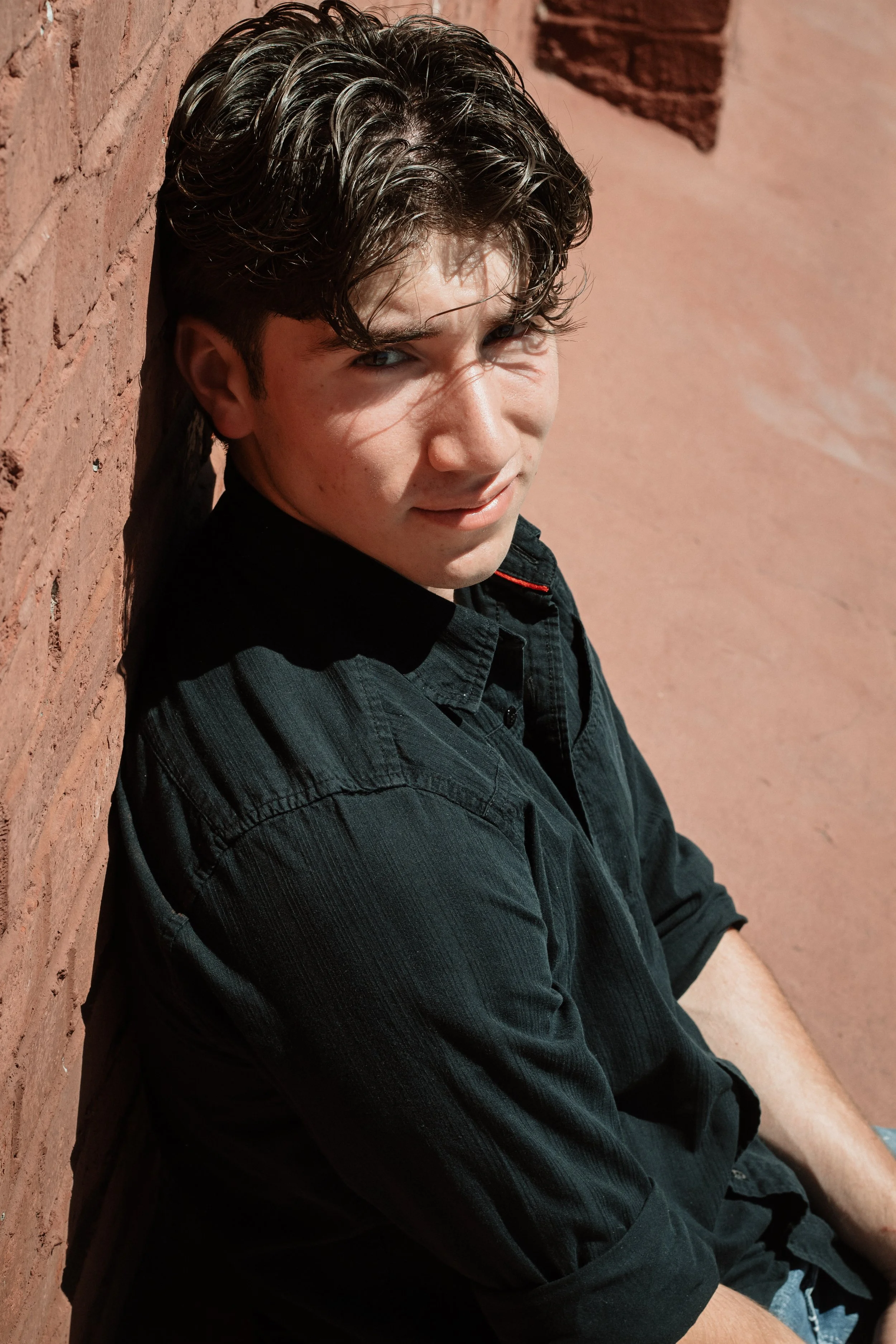 Person with black shirt leaning against a brick wall outdoors.