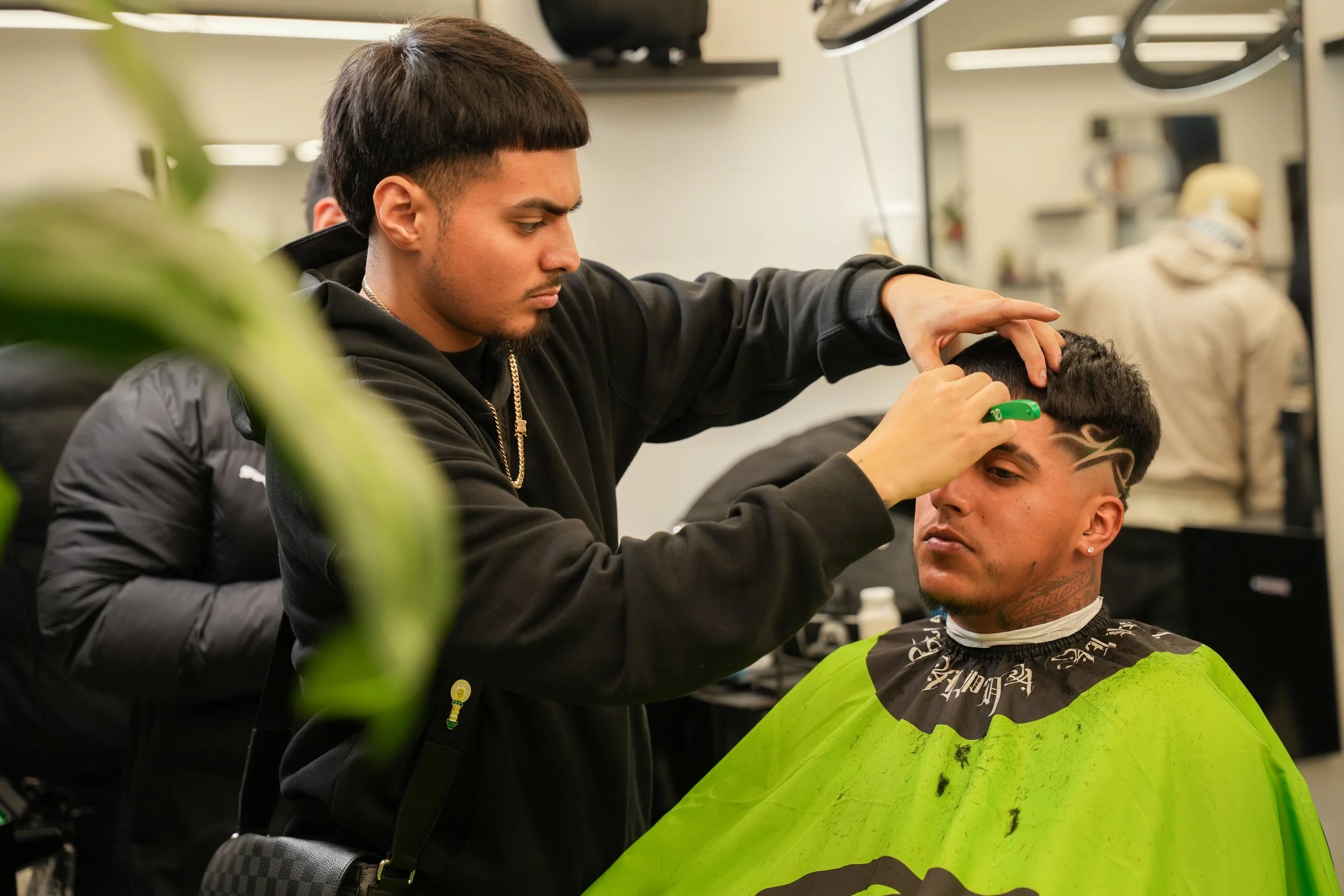 A barber Chuy Blendz styling a man's hair with a trimmer in a Suave barbershop Windsor Ca.
